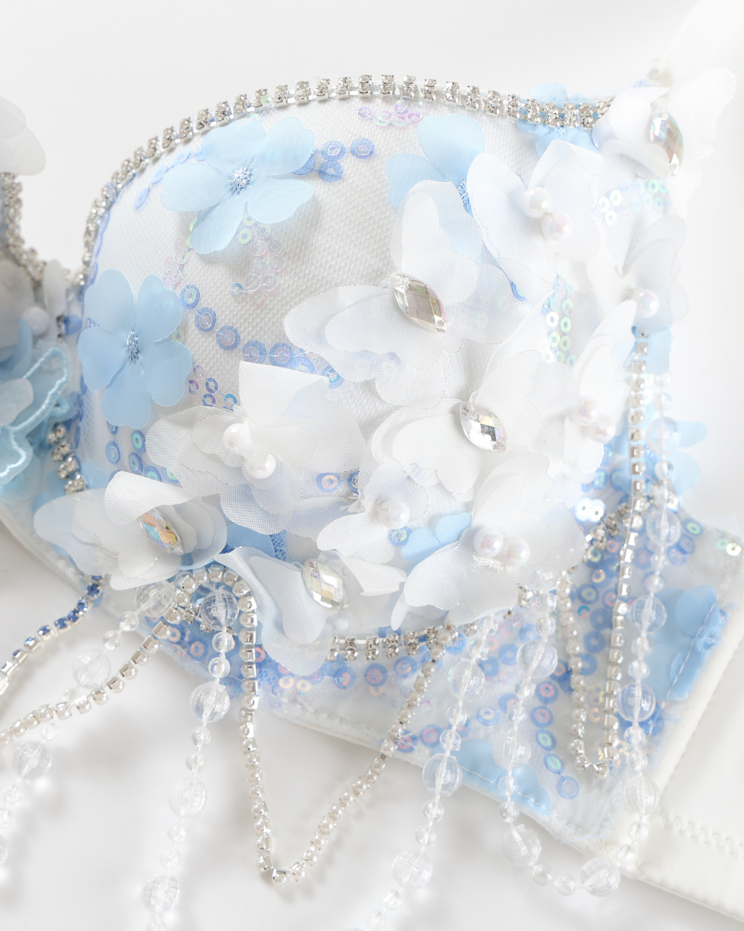 Close-up of the Icemuse - Blue - Top featuring blue and white 3D floral appliqués, clear beads, sequins, and rhinestone chains, set against a white background.