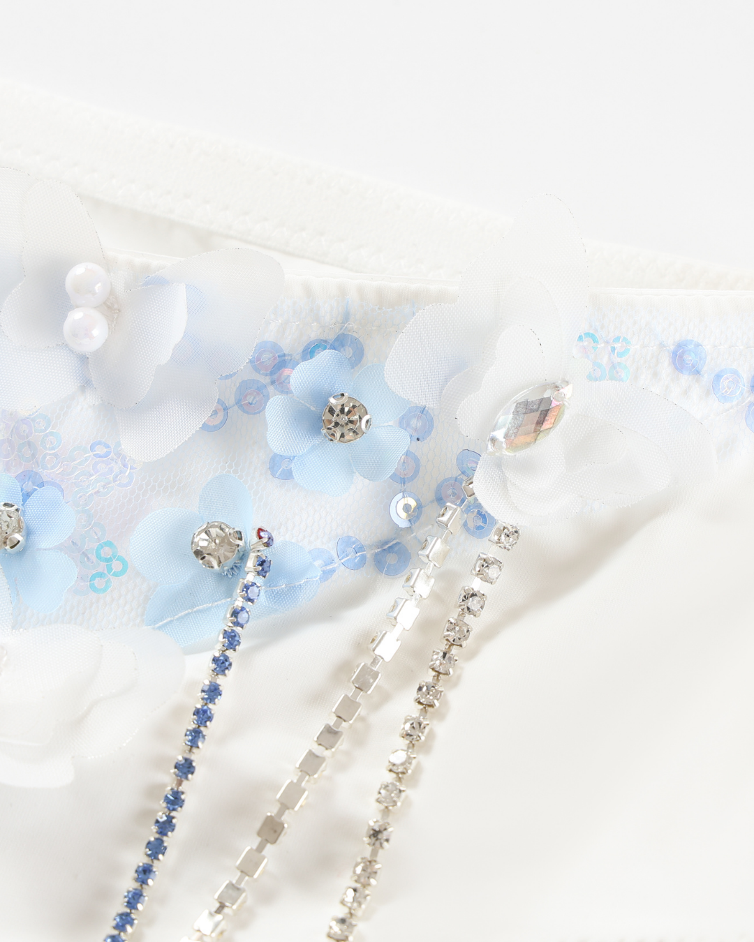 Close-up of Icemuse - Blue - Bottom, featuring white fabric adorned with blue and white flowers, pearls, sequins, rhinestones, and silver beaded strands.