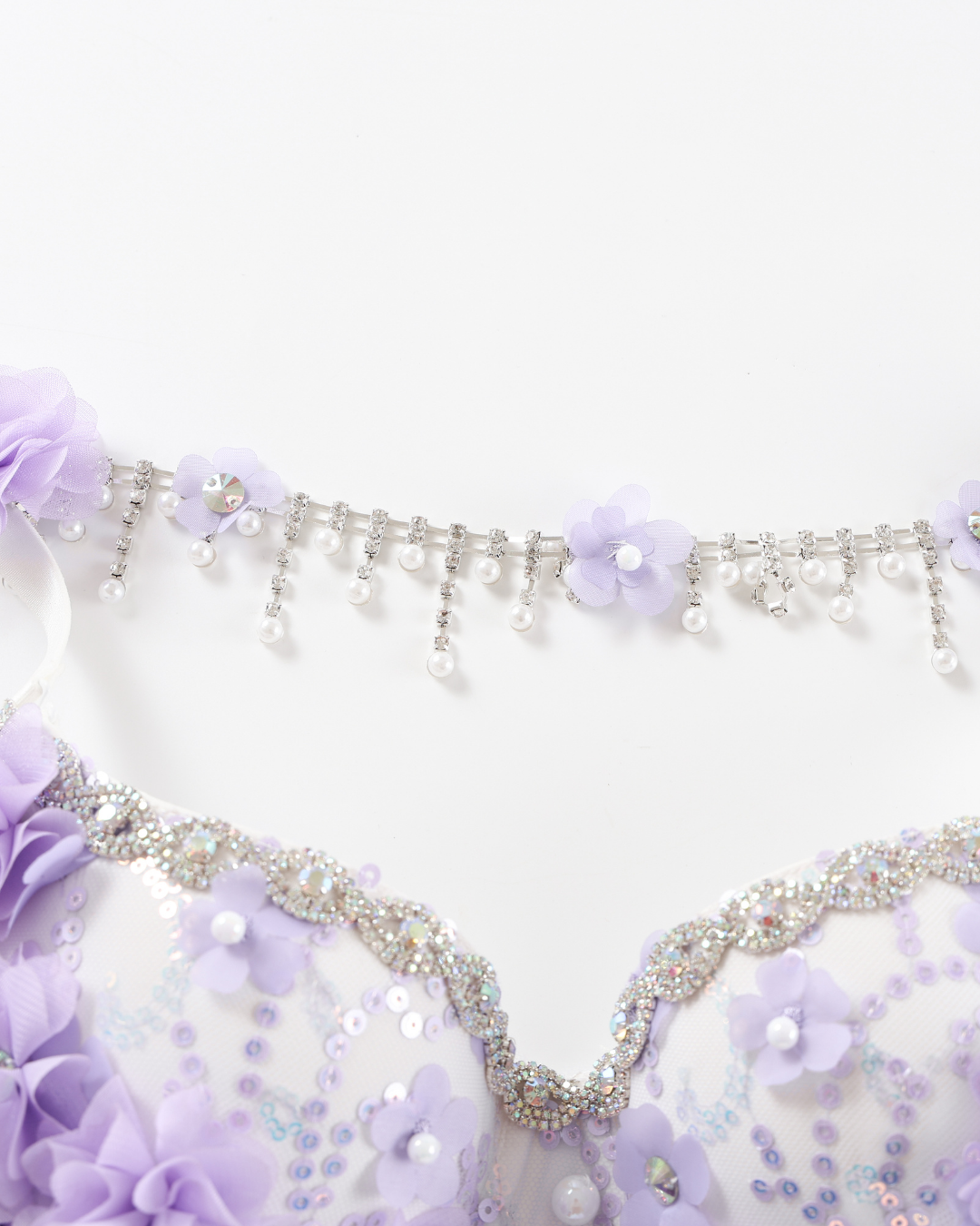 Close-up of the Lavendelle - Purple - Top, showcasing purple fabric flowers, sequins, beads, and a silver chain with dangling pearls on a white background.