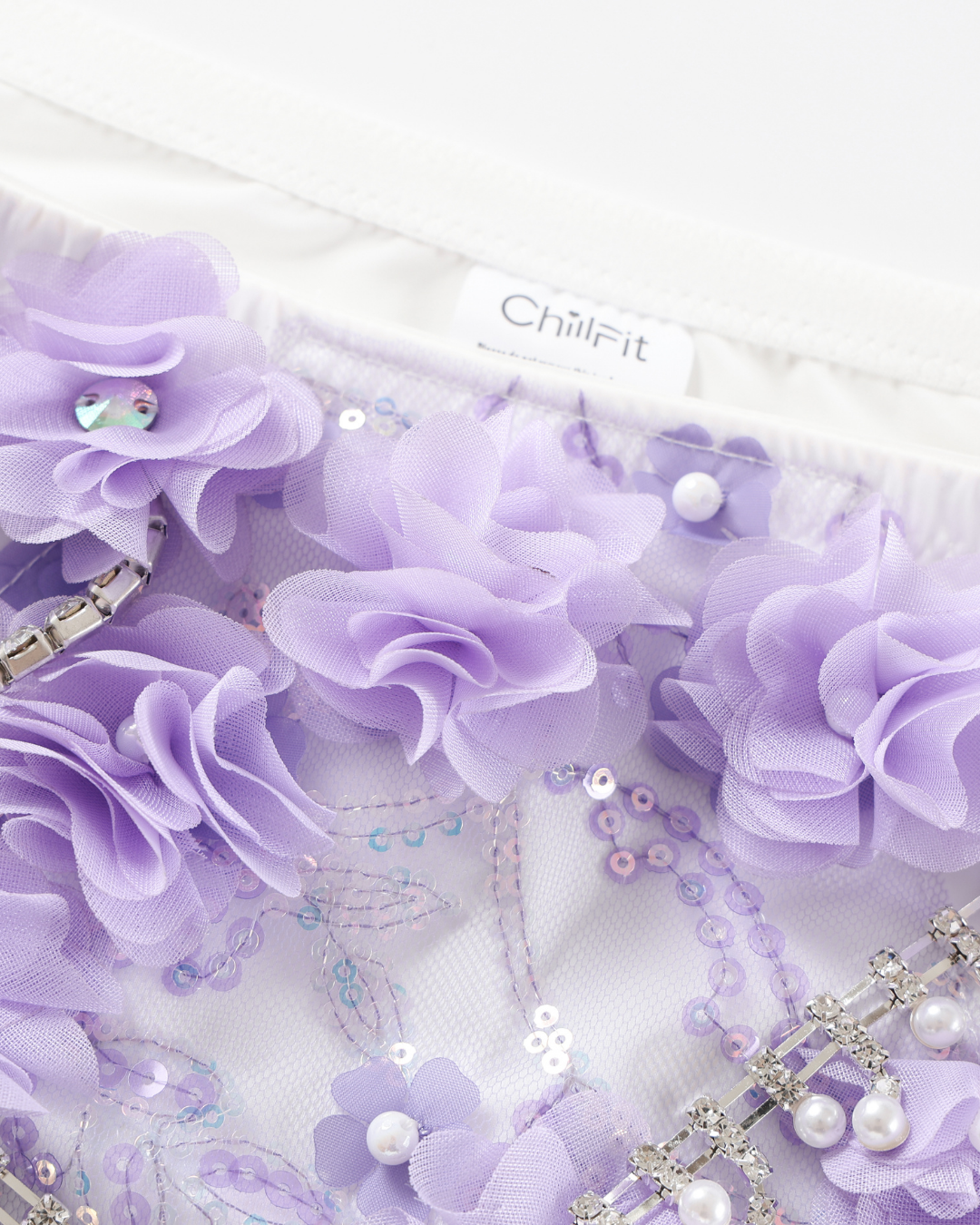 Close-up of Lavendelle - Purple - Bottom, showcasing lavender fabric flowers, sequins, pearls, and decorative rhinestones on sheer material.