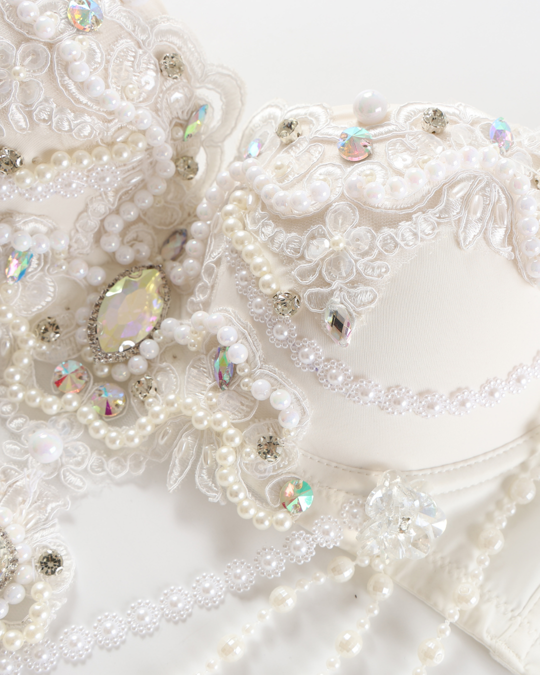 Close-up of the Opheline - White - Top, a decorative white item featuring lace, pearls, sequins, beads, and crystal-like embellishments against a white background.