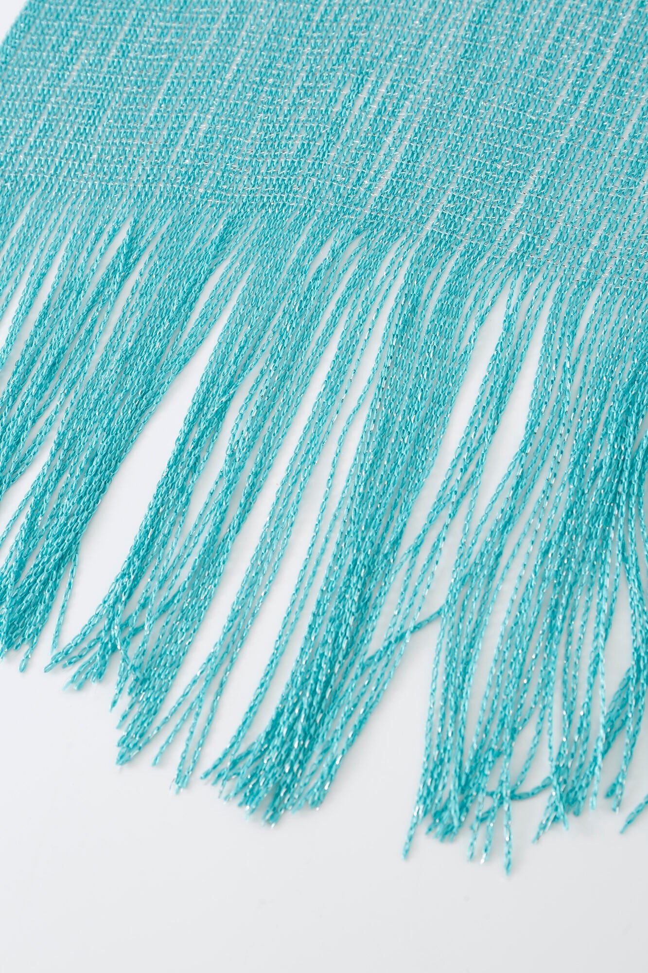 Close-up of the Pashmina - Aqua Solid Fringe, showing its turquoise fabric and long, thin fringe strands draped on a white surface.