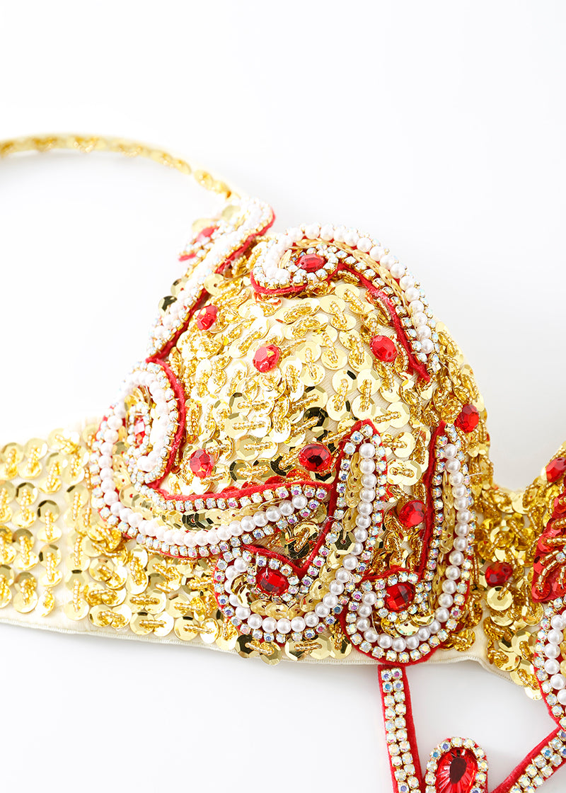 A close-up of the Imperya - Gold - Top, featuring sequins, pearls, and red and white beadwork in swirling patterns on a white base—ideal for festival wear.