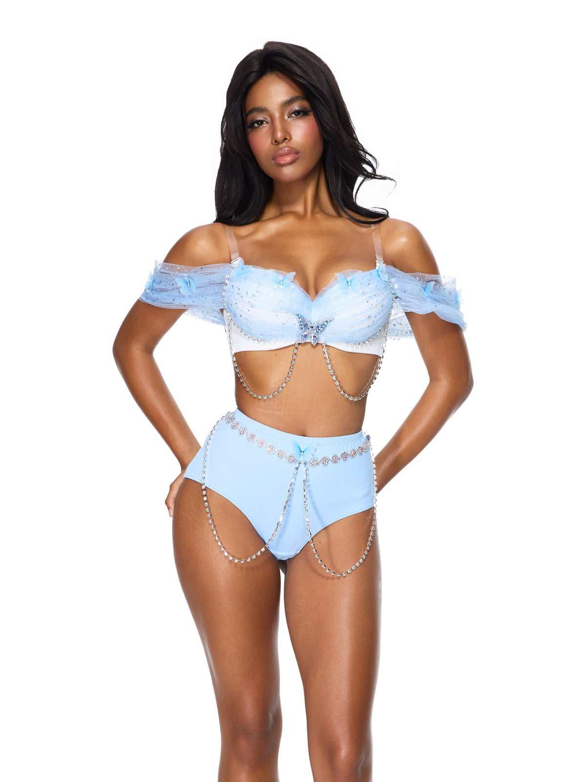 Wearing the “Dream from the Sky - Full Set - White Blue,” a light blue off-shoulder bra top paired with high-waisted shorts adorned with chain and bead embellishments, she stands against a white background—showcasing a stunning handmade rave wear look perfect for any festival.