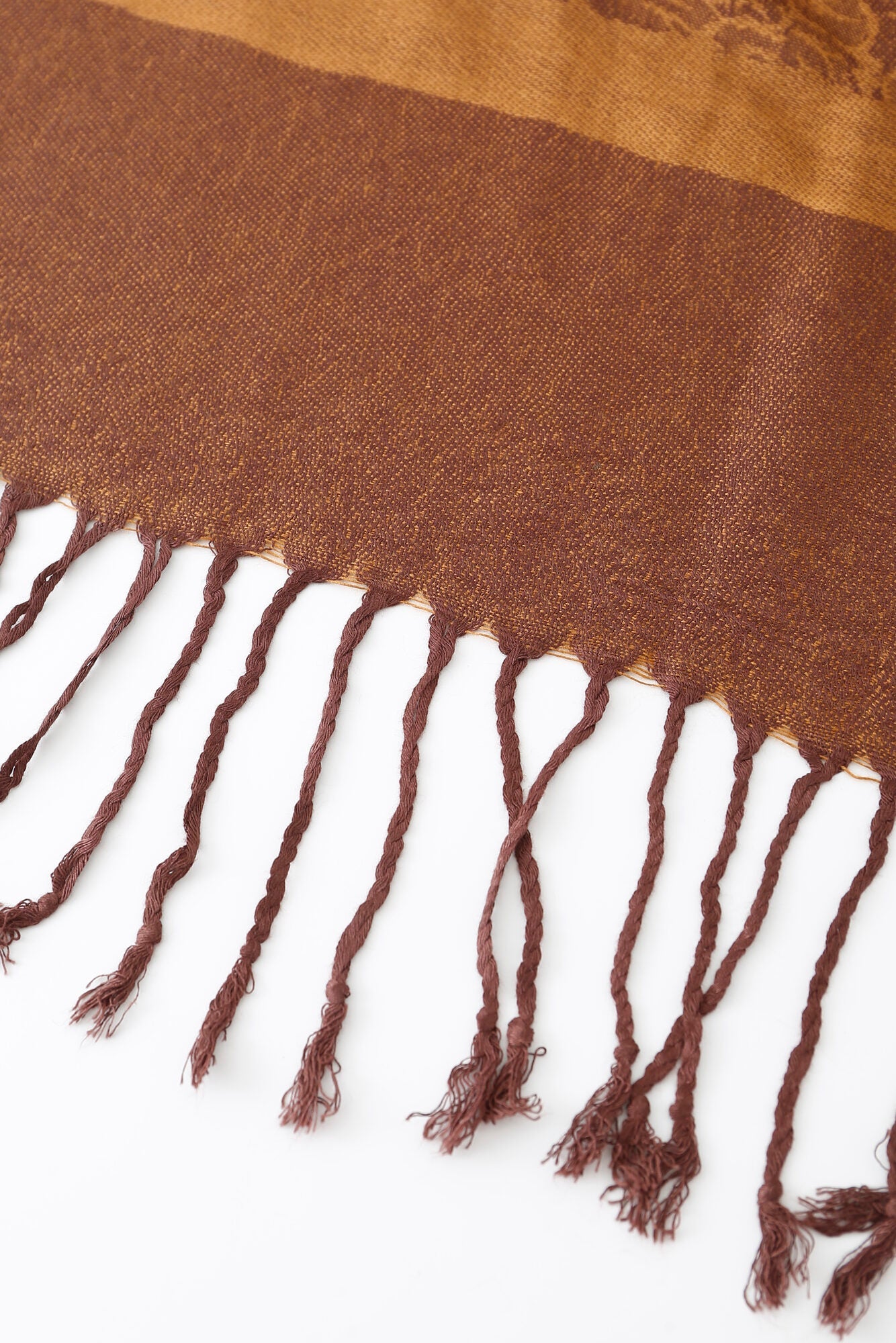Close-up of the Pashmina - Caramel Paisley Fringe, featuring brown woven fabric with twisted fringe along the edge, displayed on a white surface.