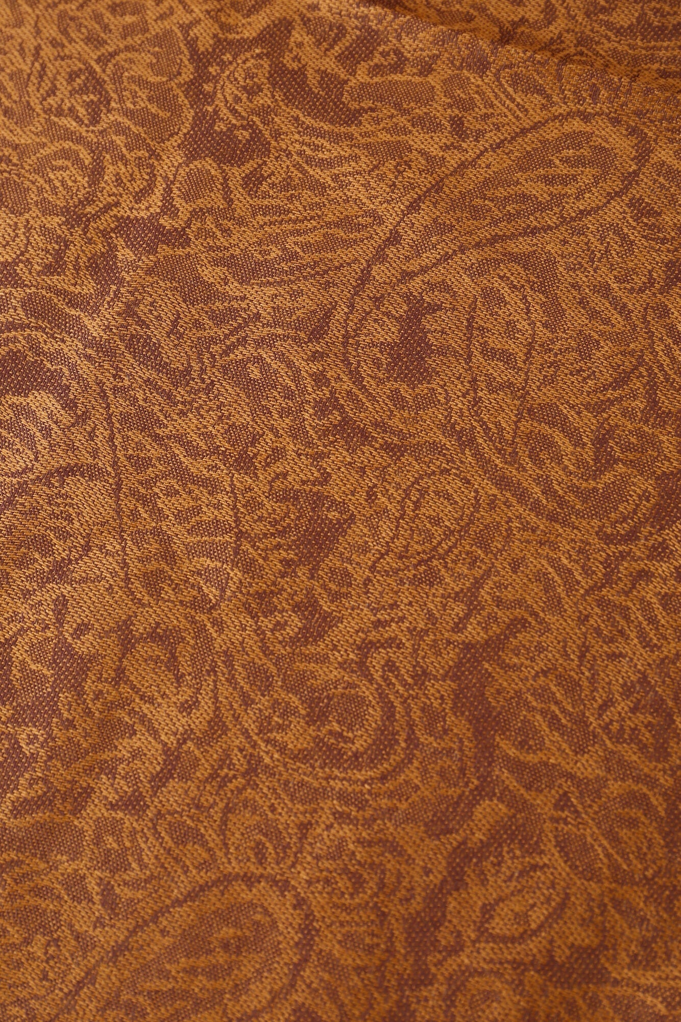 The Pashmina - Caramel Paisley Fringe features caramel brown fabric with an intricate paisley pattern of swirling shapes and fine details, finished with elegant fringe.
