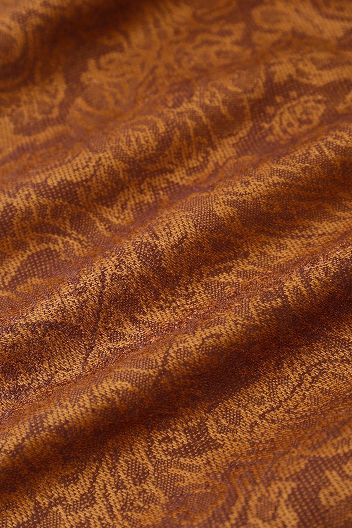 Close-up of the Pashmina - Caramel Paisley Fringe, featuring a brown and gold paisley pattern with a textured, woven look and a slightly wavy surface.