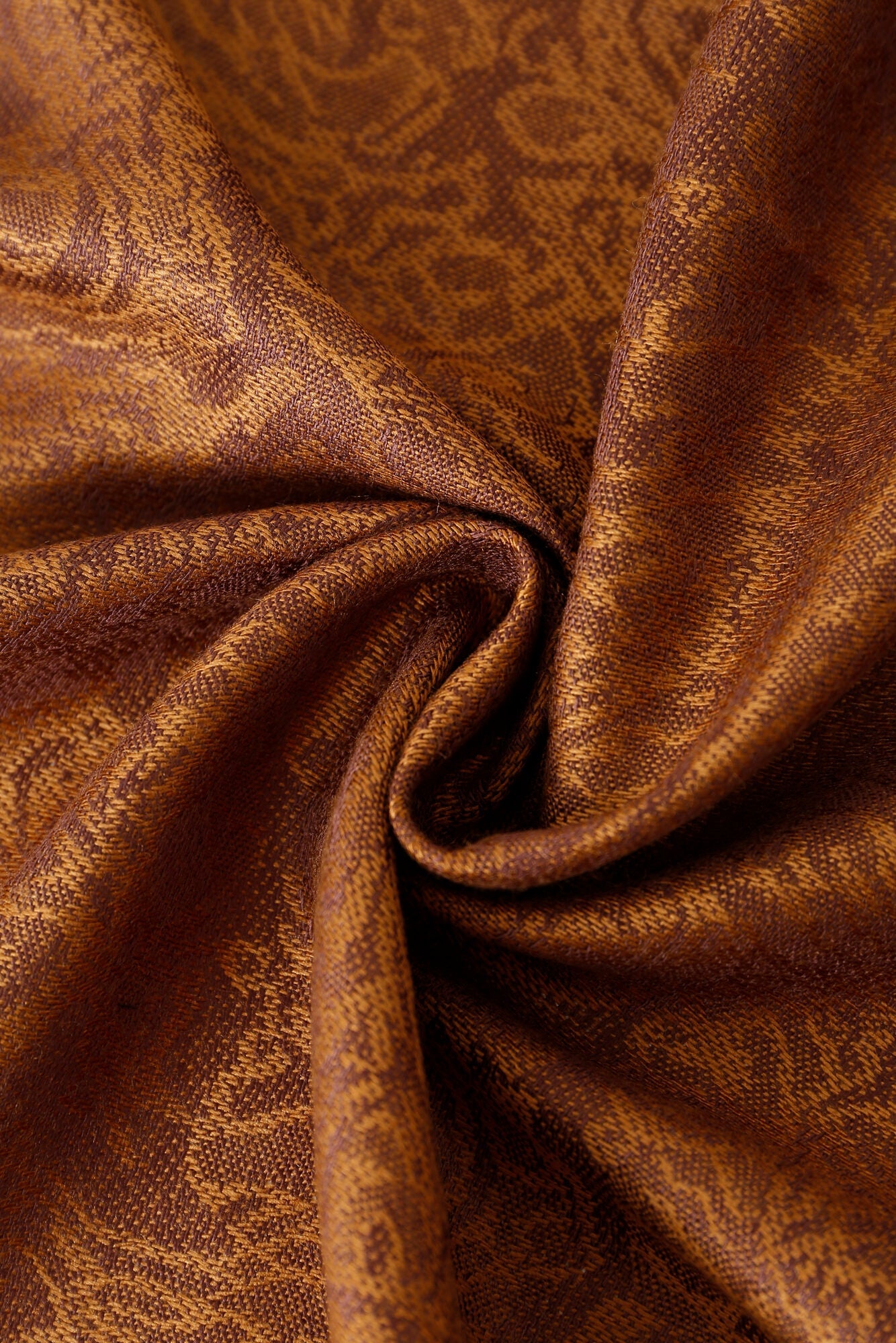Close-up of the Pashmina - Caramel Paisley Fringe, featuring textured brown and gold fabric with an intricate paisley pattern, gathered into a loose spiral fold.