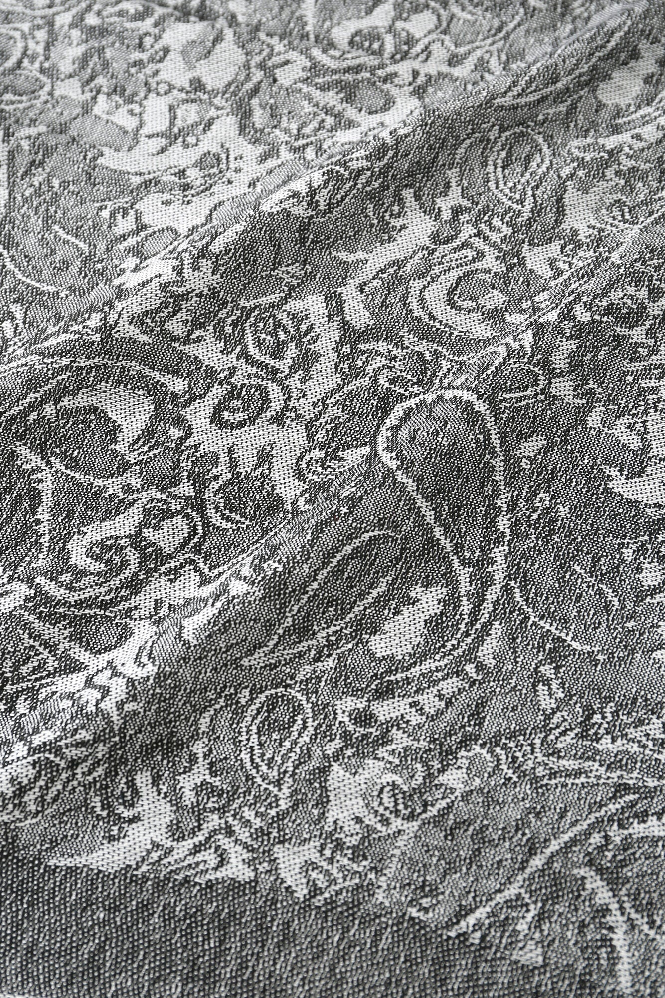 Close-up of the "Pashmina - Charcoal Bloom Fringe" shows grey woven fabric with an intricate paisley and floral jacquard pattern in light and dark tones.