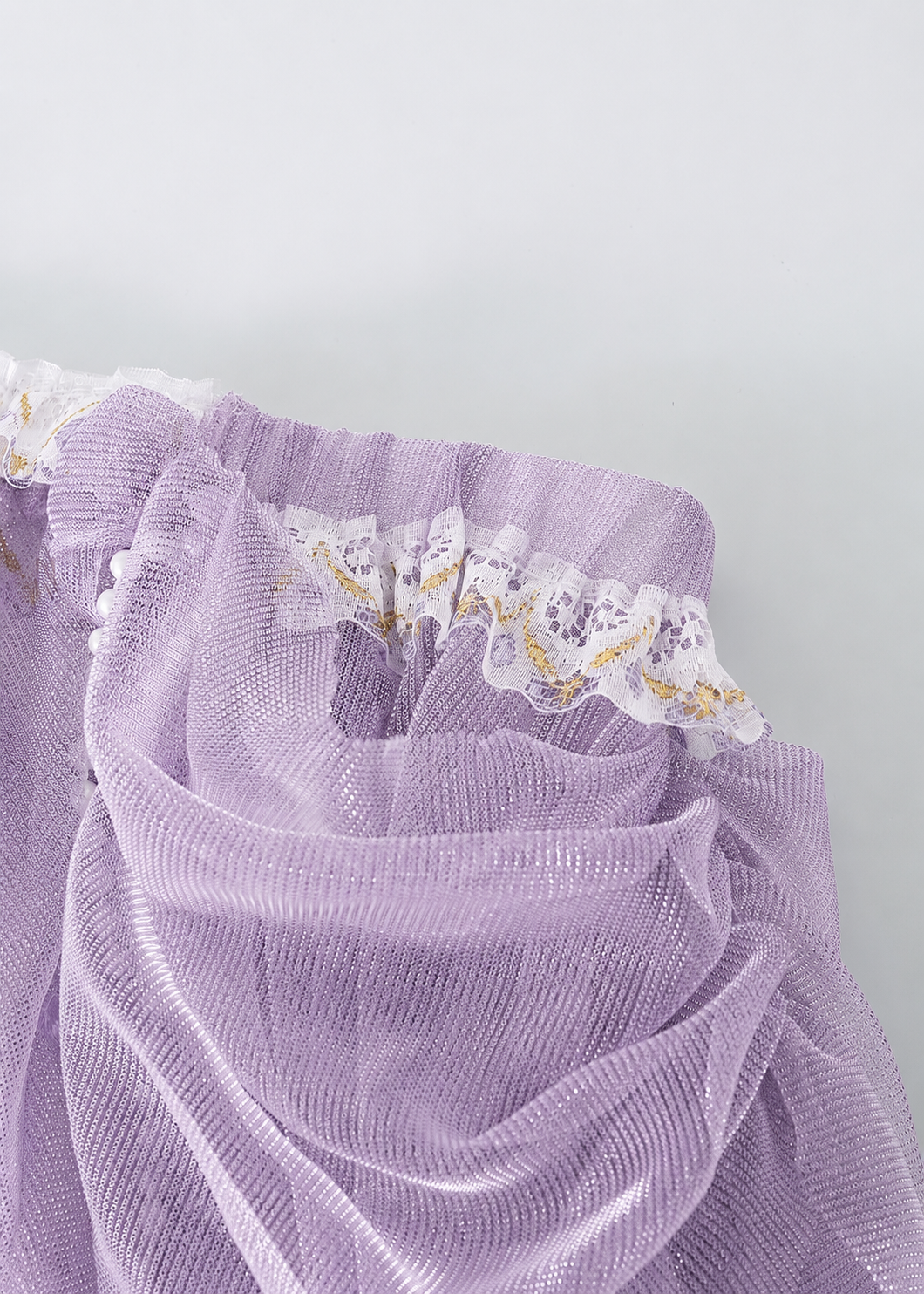 Close-up of the Gossamer-Purple-Skirt, crafted from lilac sheer fabric with delicate lace trim and white and gold accents, displayed in softly gathered folds against a light background—ideal for festival or rave wear.