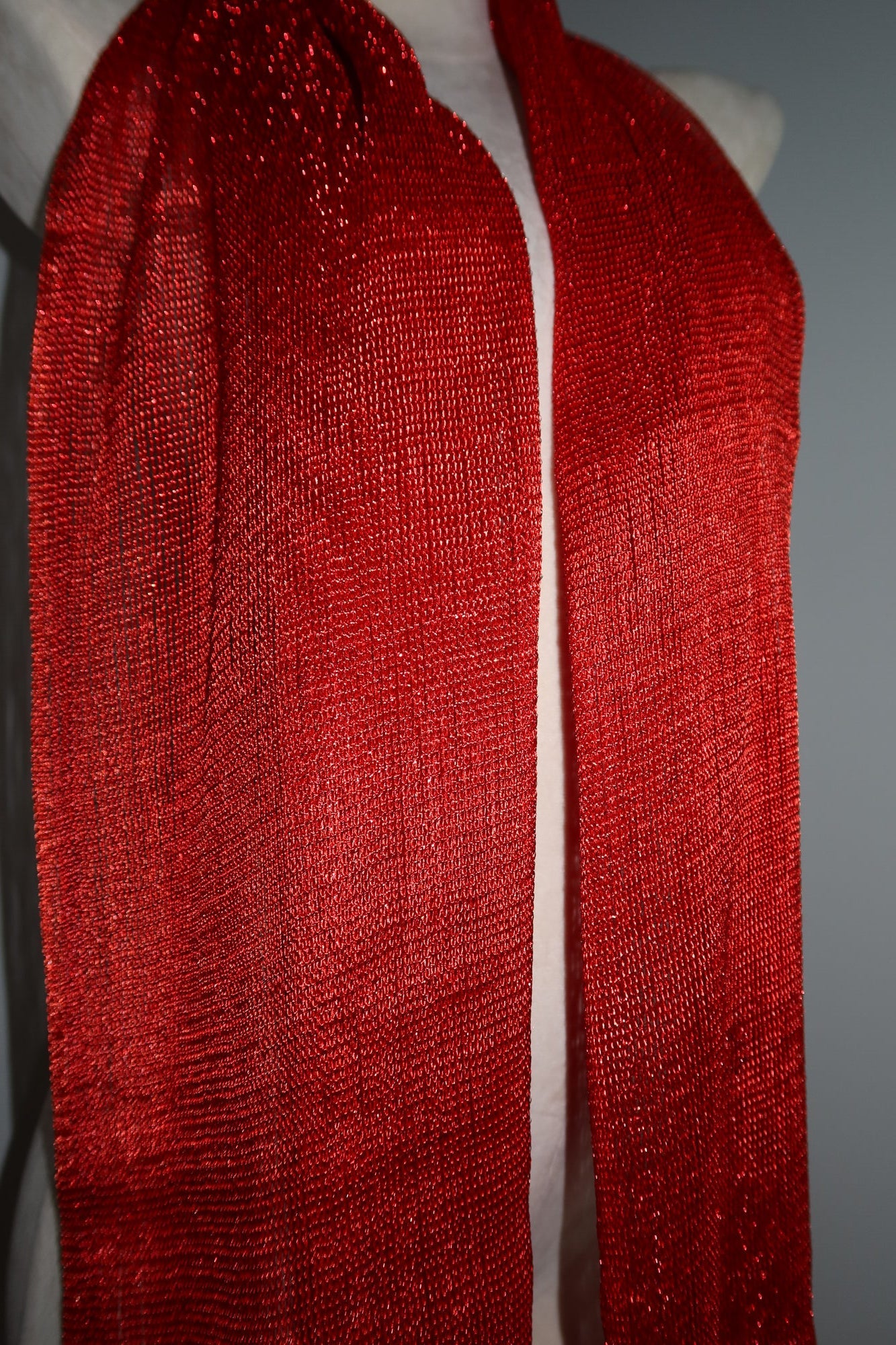 A close-up of a mannequin showcases the Pashmina - Scarlet Fringe, a long, textured, shiny red scarf against a plain background—a bold festival wrap to elevate your style.