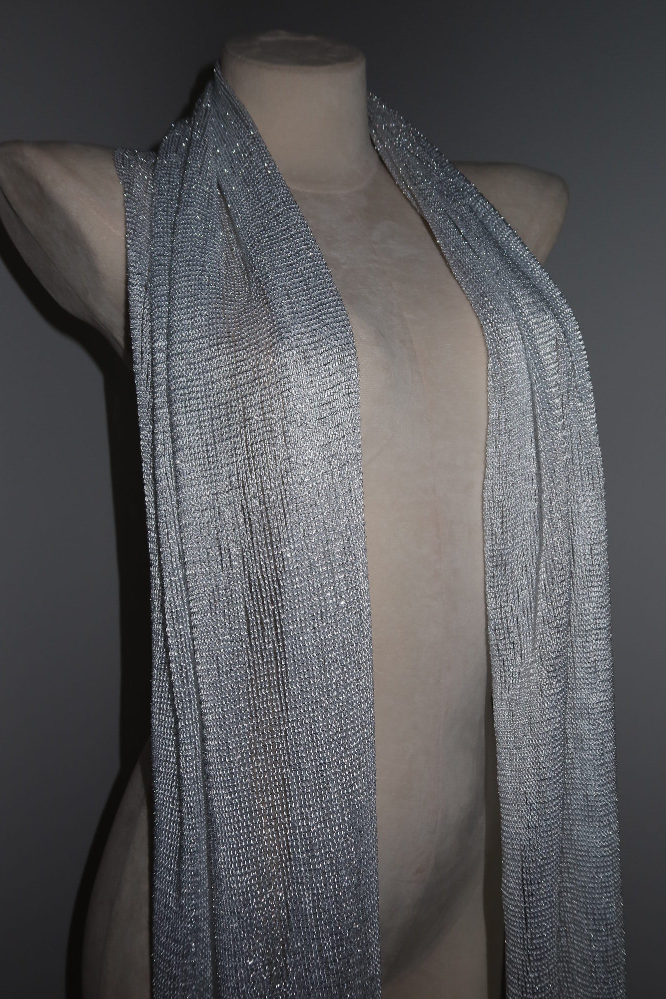 The Pashmina - Silver Sheer Fringe drapes elegantly over a nude mannequin torso against a dark background—ideal for making a bold statement at music festivals.