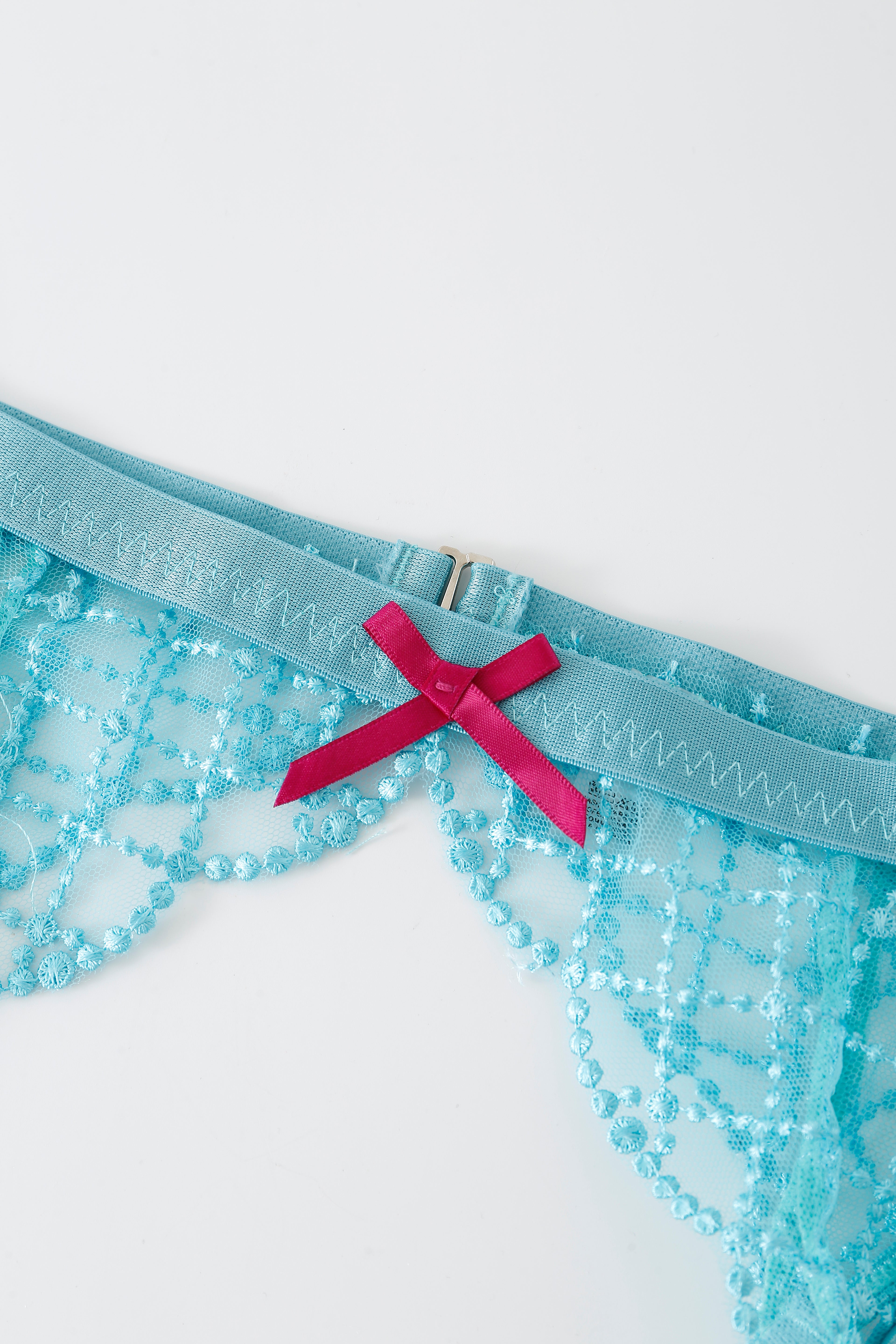 Close-up of the Lagoon w Pashmina- Full Set lingerie in blue lace, featuring a decorative pink bow and zigzag stitching detail on a white background.