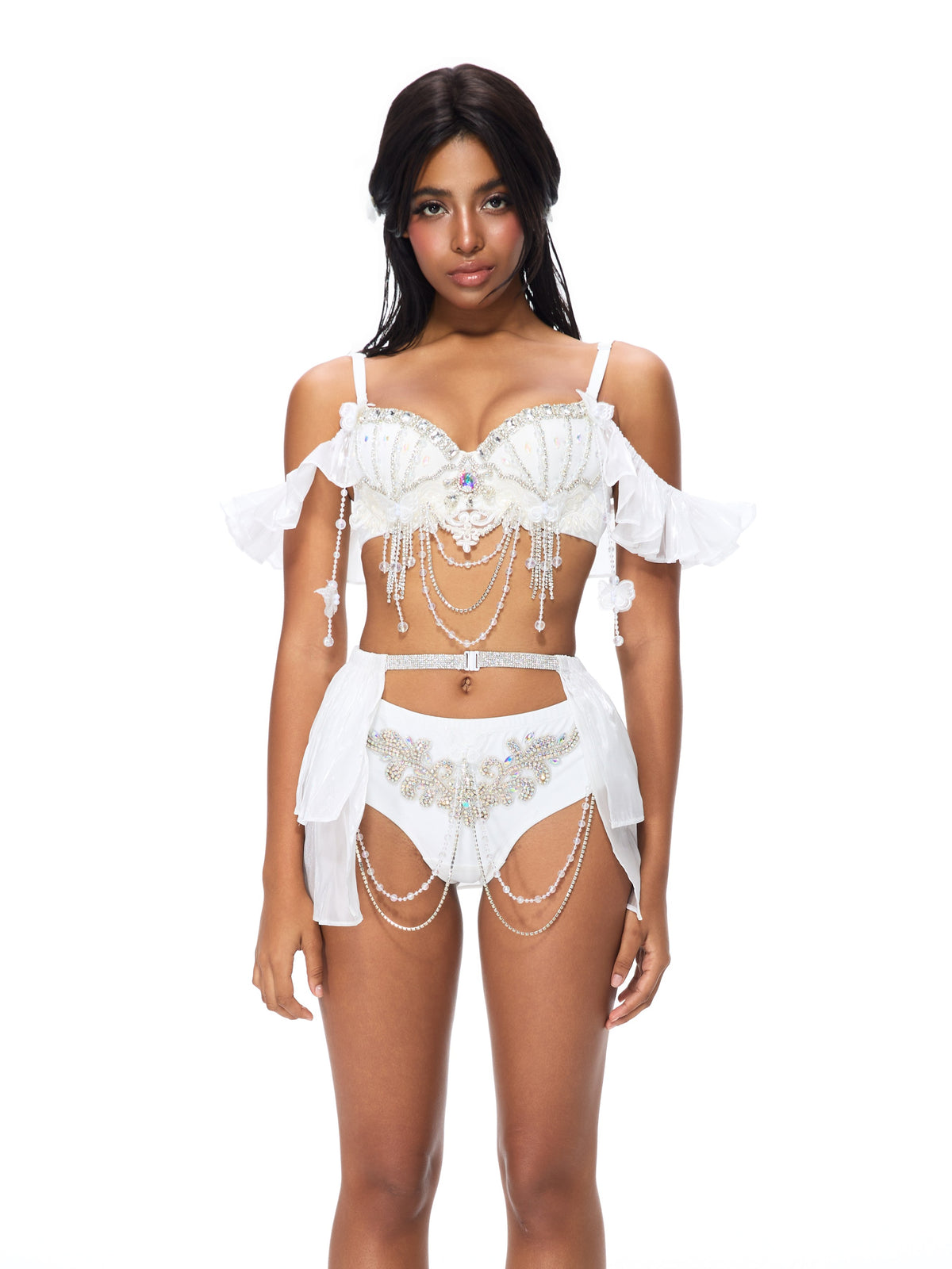 A woman stands against a white background wearing the Pearl Wing - Full Set - White, an embellished lingerie ensemble featuring a satin push-up bra top adorned with pearls, beads, and draped chains—a stunning example of handcrafted festival wear.
