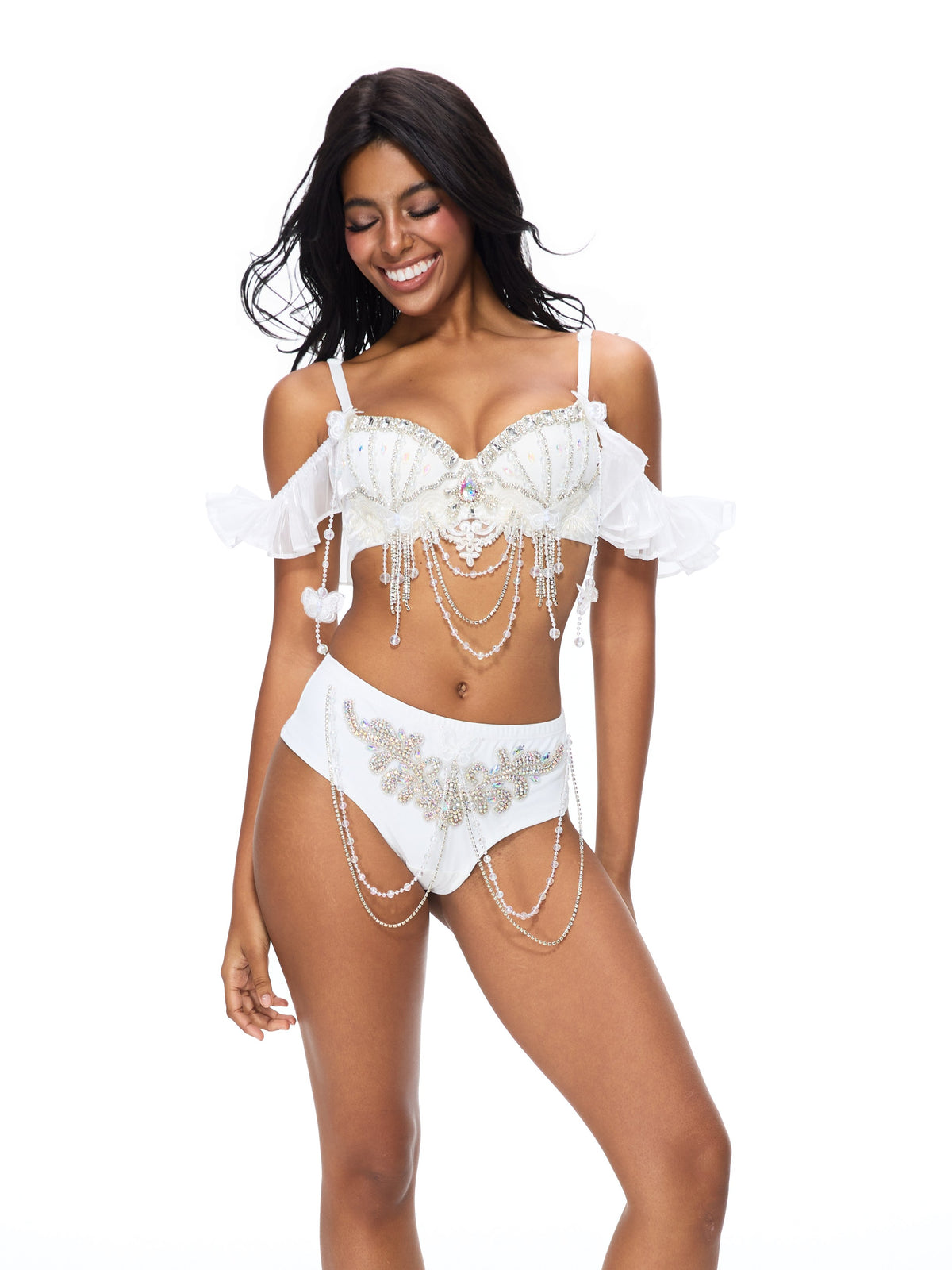 A woman stands smiling against a plain white background, showcasing the Pearl Wing - Full Set - White: an exquisitely handcrafted lingerie ensemble adorned with pearl embellishments and delicate ruffles—perfect as standout festival wear for your next rave.
