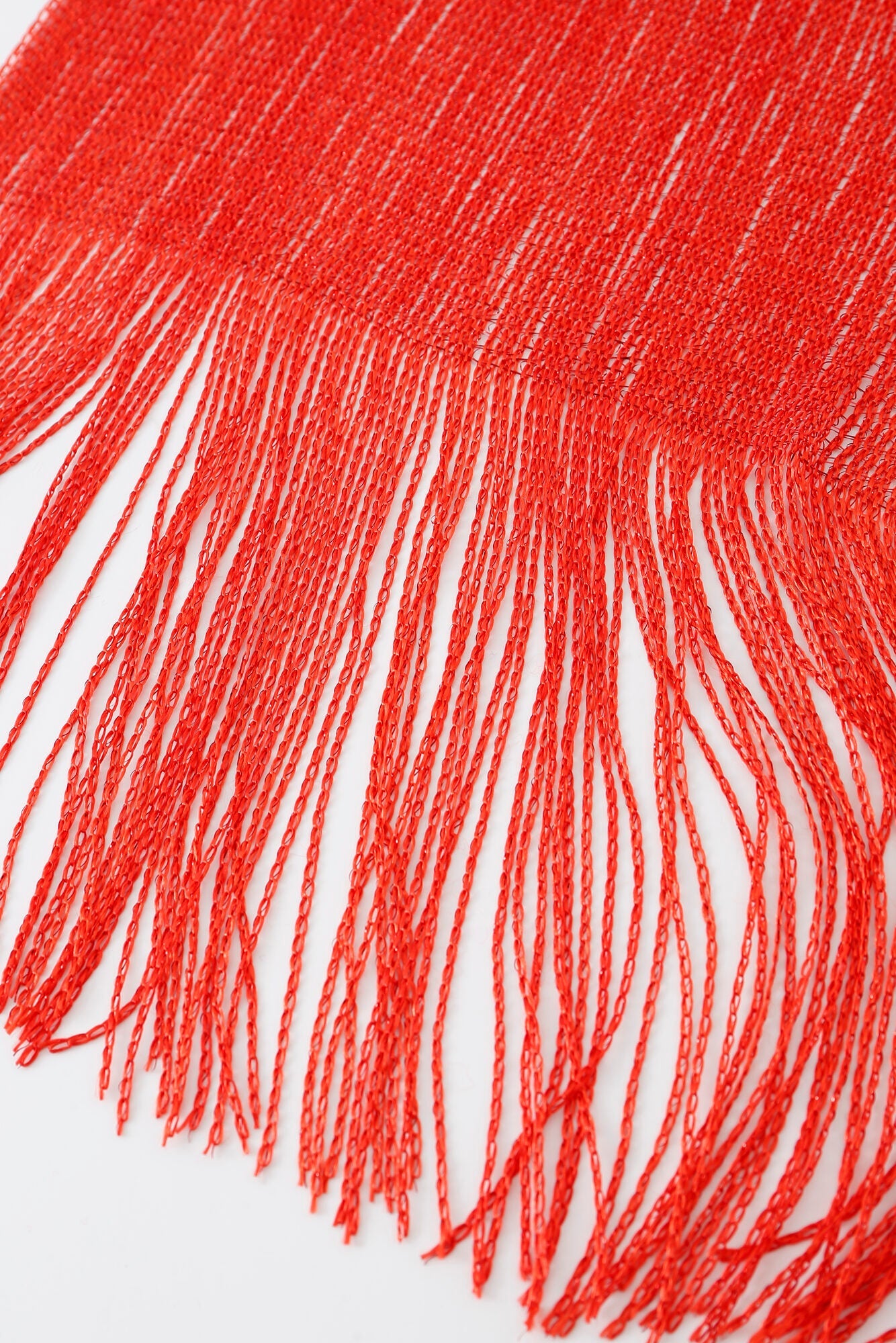 Close-up of the Pashmina - Scarlet Fringe, highlighting its red fringed edge with numerous threads extending against a white background.