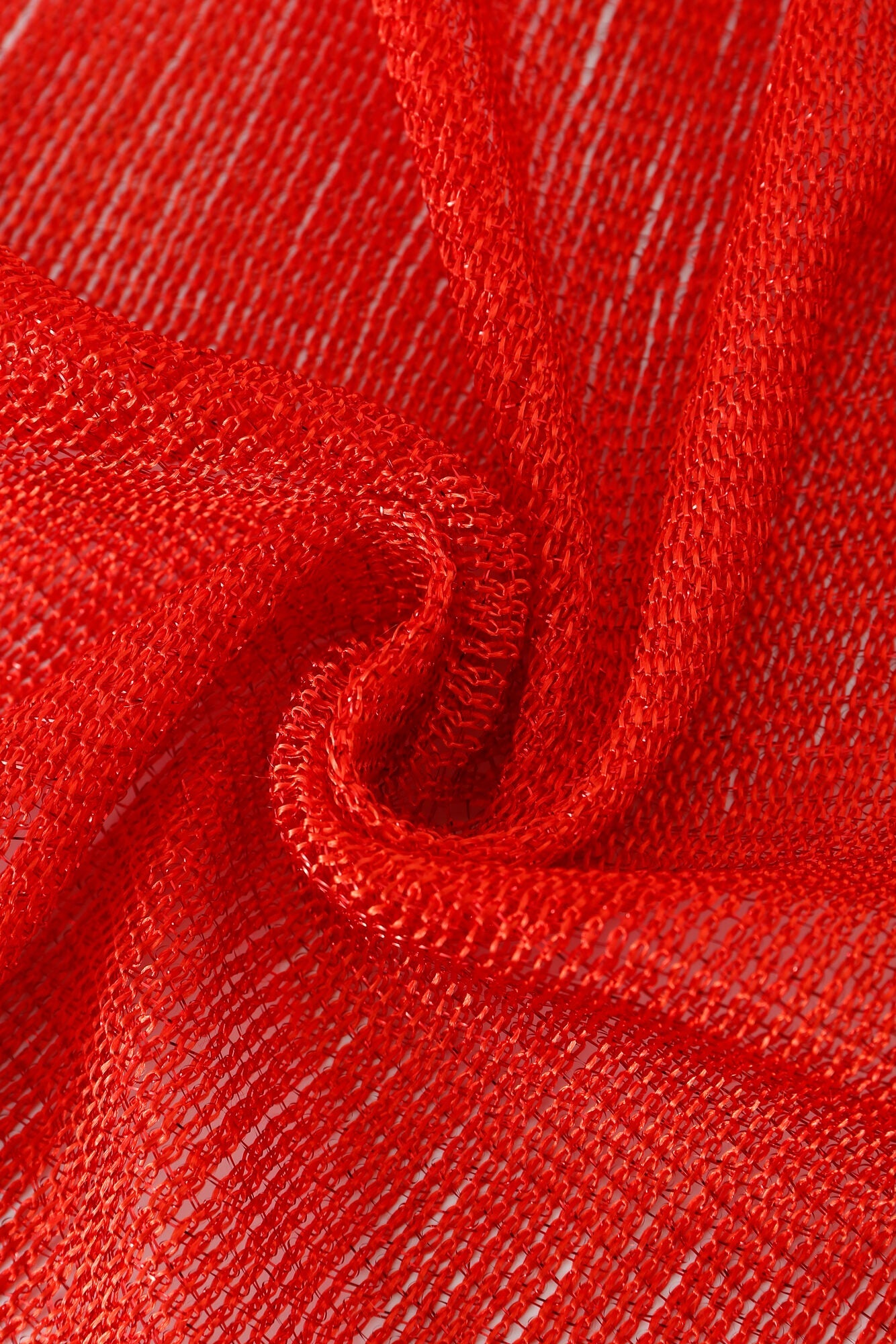 Close-up of Pashmina - Scarlet Fringe, showcasing its sheer red fabric with a loose, open weave texture, gently folded and arranged in an elegant swirl pattern.