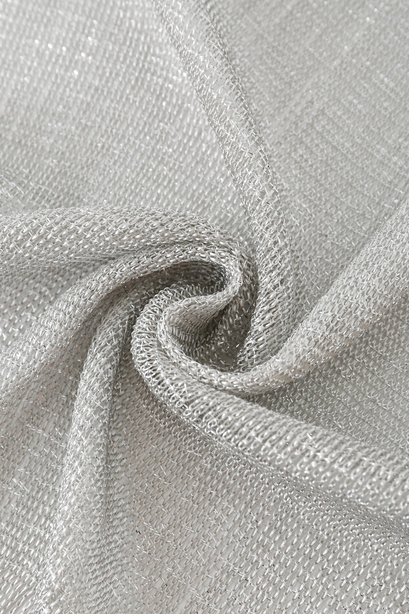 Close-up of Pashmina - Silver Sheer Fringe fabric twisted into a spiral, featuring a loose open weave and subtle shimmer in its silver metallic threads.