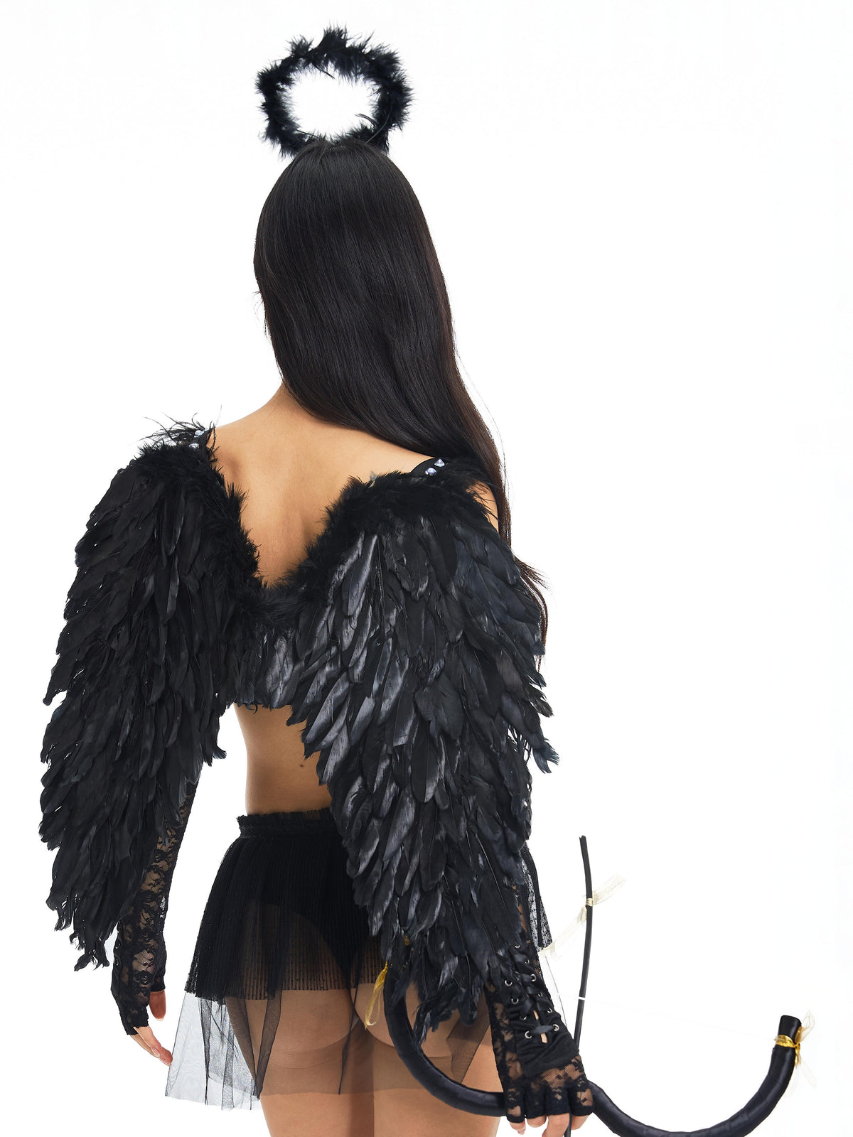 A person wearing the Haló- Skirt- Black, styled with black feathered wings, a black halo headband, hand-sewn pearls on delicate black lace gloves, and holding a black bow, is photographed from behind against a white background.