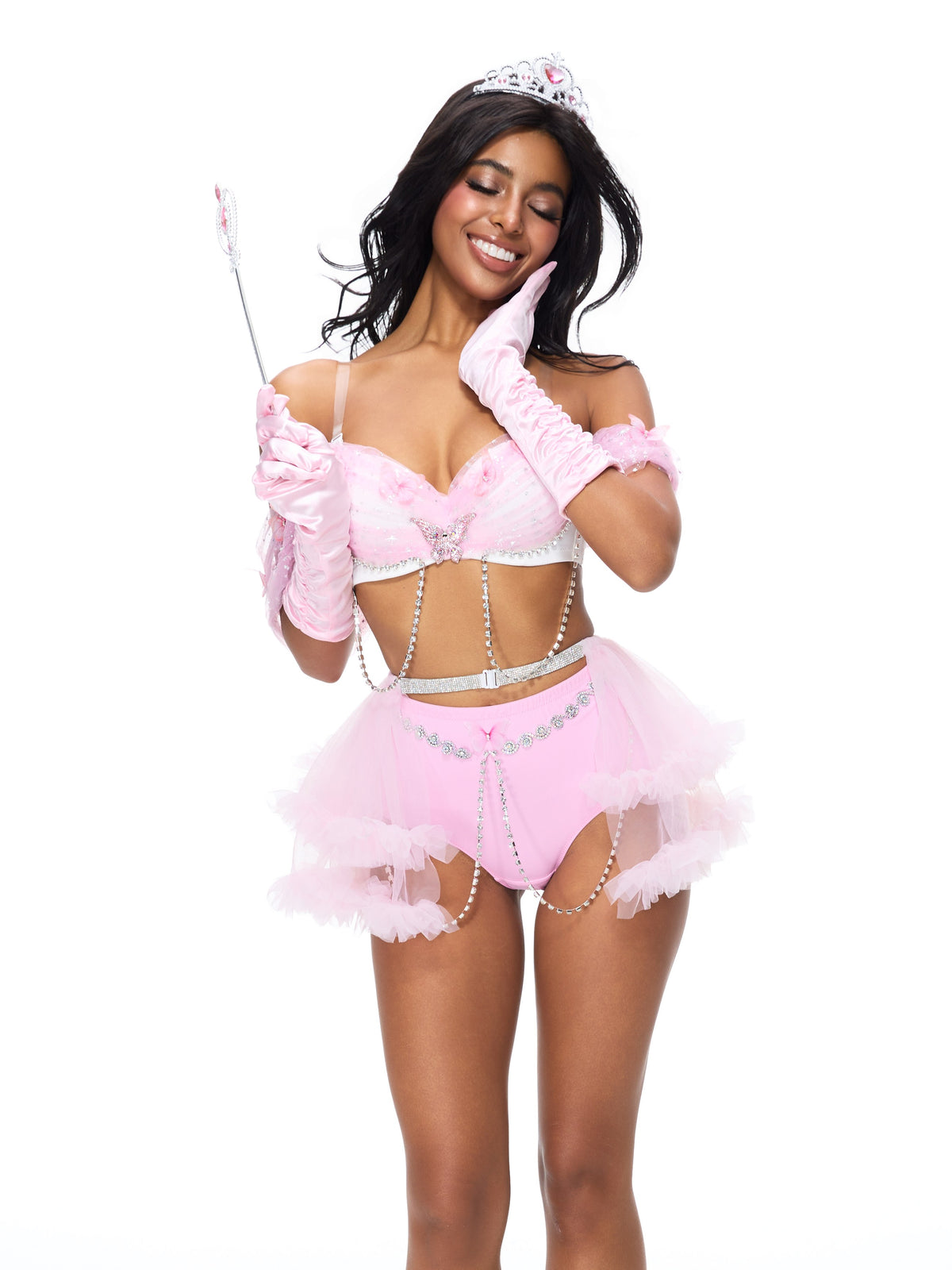 A woman is smiling brightly, one hand touching her cheek, while wearing the Princess 2 Pieces Set- Pink—complete with sparkling tiara and wand—against a white background, making it an enchanting choice for anyone in search of festival costume accessories.