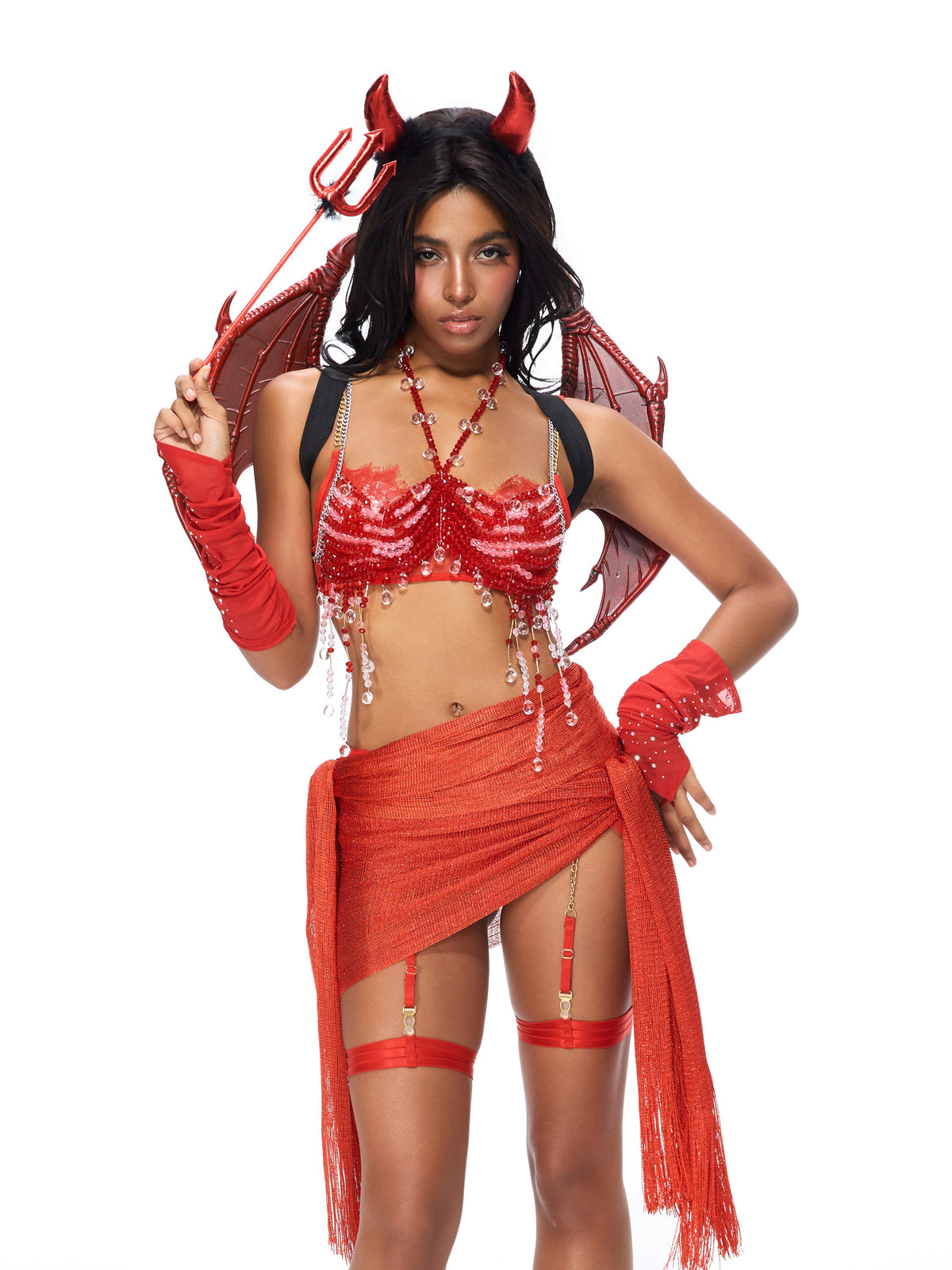Sure! Here’s the rewritten sentence using your product name: A woman in a red devil costume featuring The Sin- Poppy Red top, paired with horns, wings, a trident, a red skirt, red mesh gloves, and devil accessories, stands against a white background.
