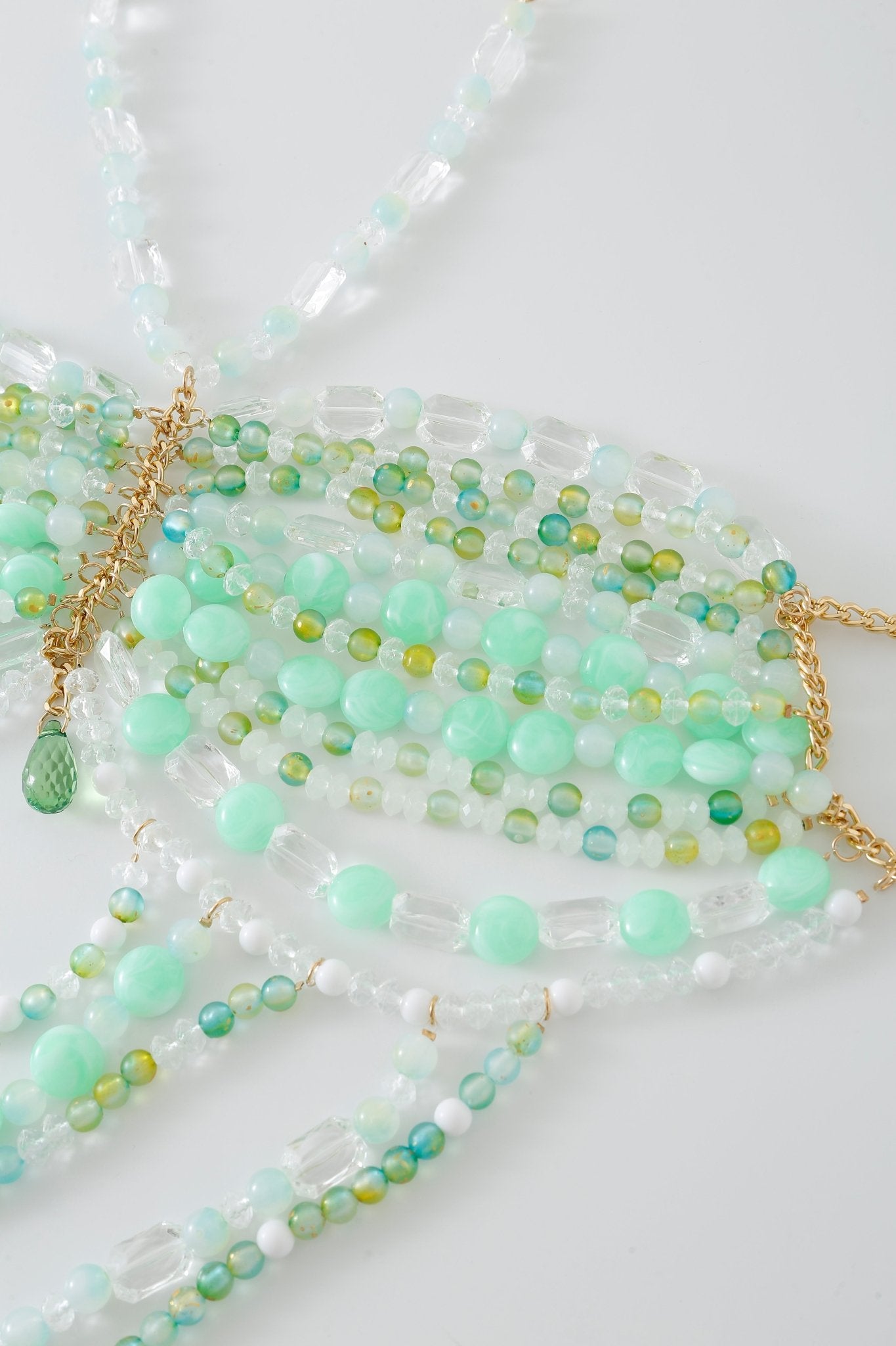 Introducing the Anemone w Pashmina- Full Set: an arrangement of beaded necklaces featuring green, blue, and clear beads accented with gold chains, all displayed on a white surface. This set is perfect for pairing with a beaded top or layering alongside your favorite fringe pashmina wrap.