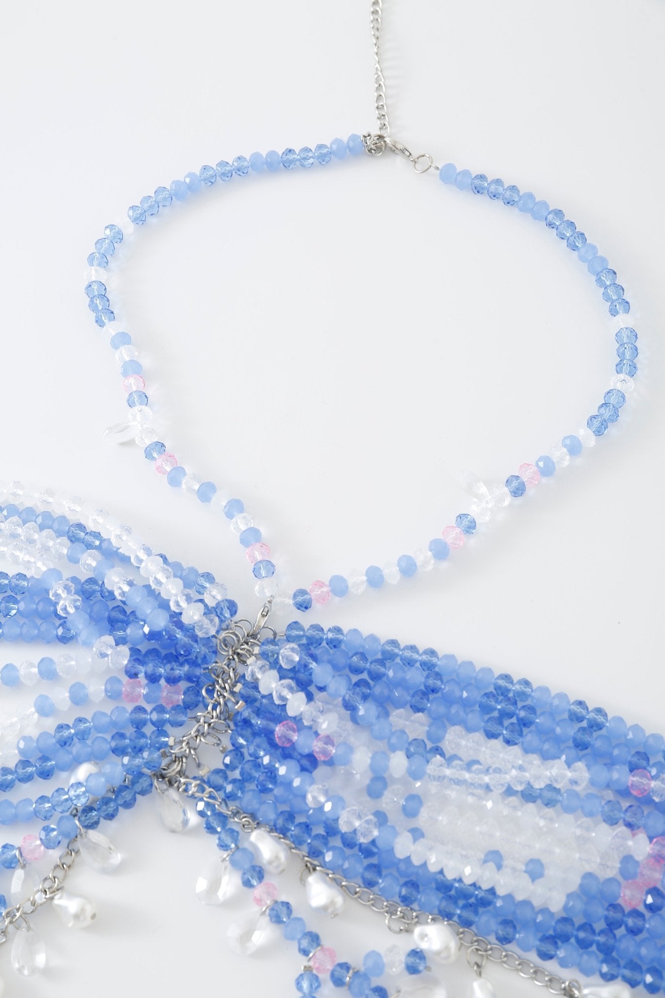 A close-up of the Azura w Mini Skirt- Full Set showcases beaded detailing with blue, white, and pink beads, silver chains, delicate rhinestone accents, and small white embellishments against a white background.