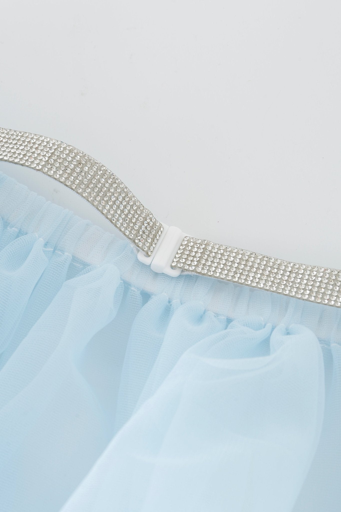 A close-up of the Azura w Mini Skirt - Full Set showcases its silver glittery belt with a white clasp attached to light blue sheer fabric, set against a white background.