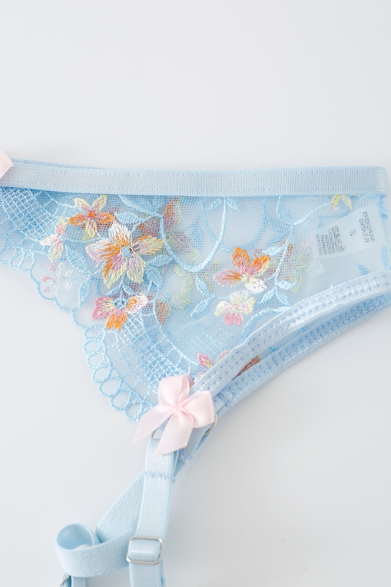 The Azura w Mini Skirt- Full Set showcases light blue lace underwear adorned with floral embroidery, pink bows, attached straps, and delicate rhinestone detailing—all presented on a white background in this signature Azura lingerie design.