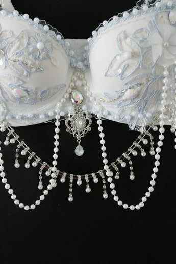 The Eira - Full Set - Blue features a white ornate bra with blue embroidery, beadwork, and dangling pearl and crystal chains, handcrafted for rave festival wear and shown against a black background.
