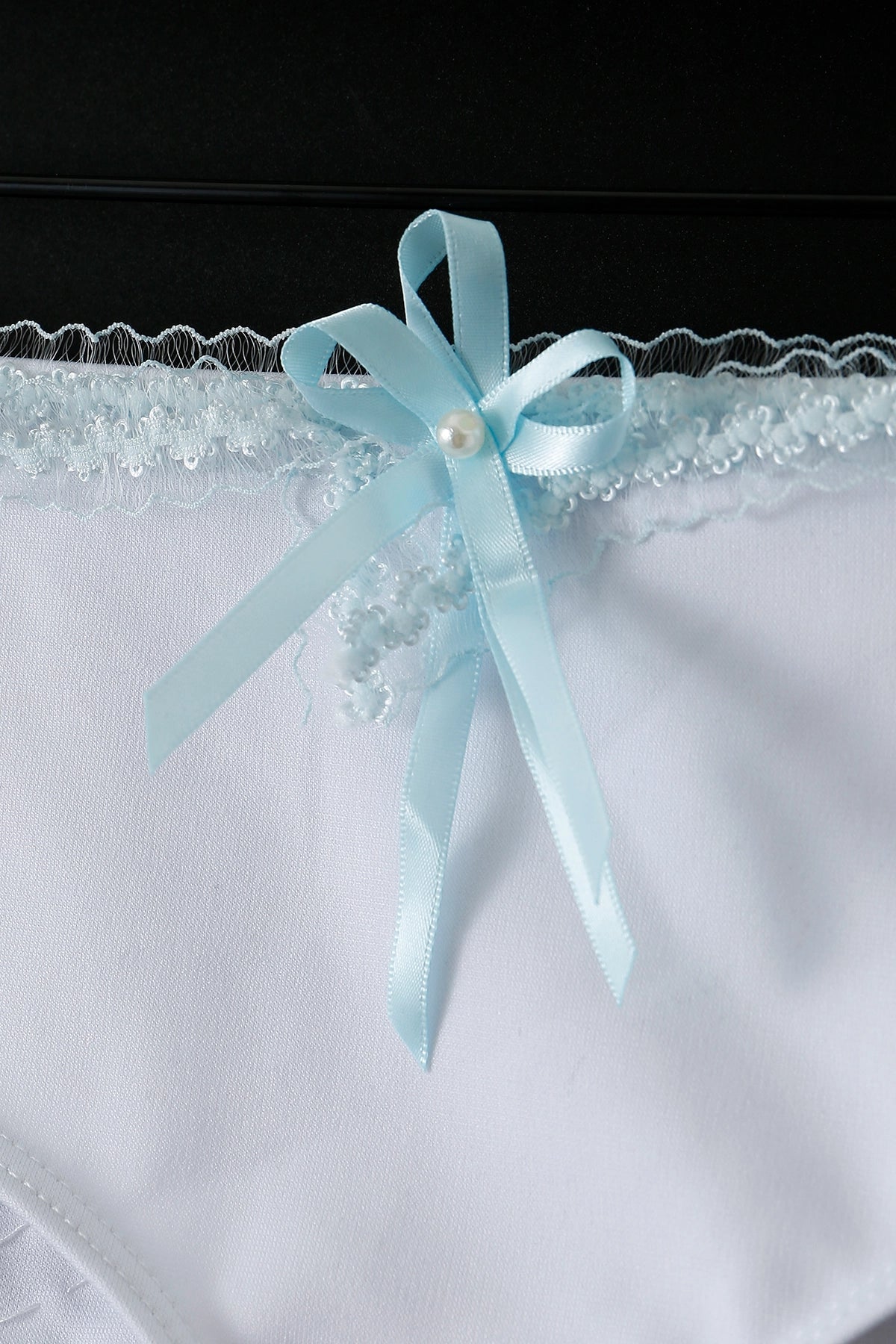 Close-up of Eira - Full Set - Blue: white lingerie with lace trim and a light blue satin bow with pearl bead, ideal as handcrafted rave outfit or delicate rave festival wear.