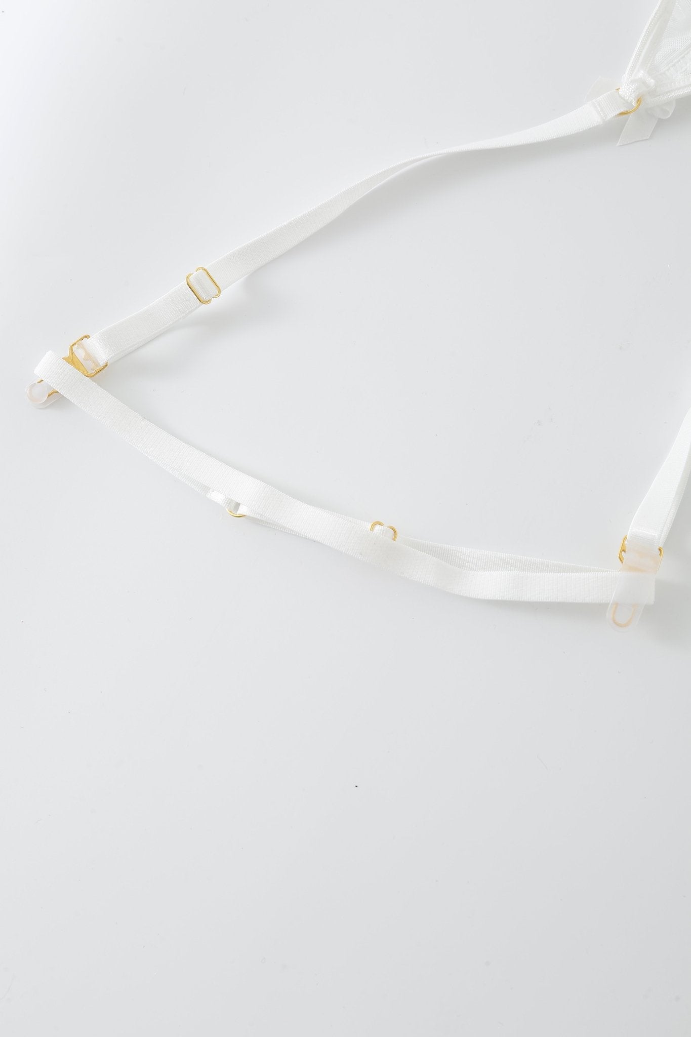 White adjustable straps with gold hardware are laid out on a plain white surface, echoing the sophisticated accents of the Eve w Mini Skirt- Full Set, renowned for its subtle rhinestone details and refined aesthetic.