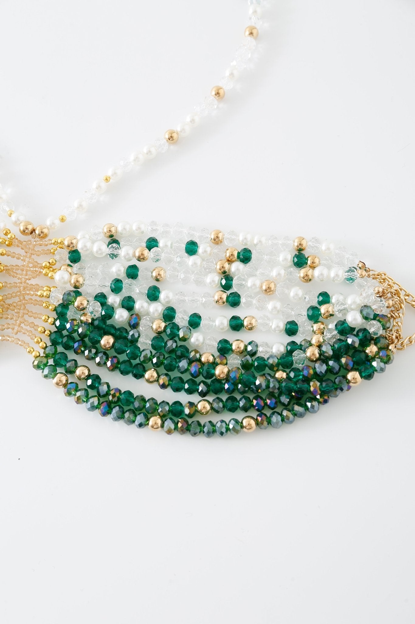 A close-up of the “Eve w Pashmina- Full Set,” showcasing its layered arrangement of green, white, and gold beads on a white background, reminiscent of the intricate detailing found on a beaded top.