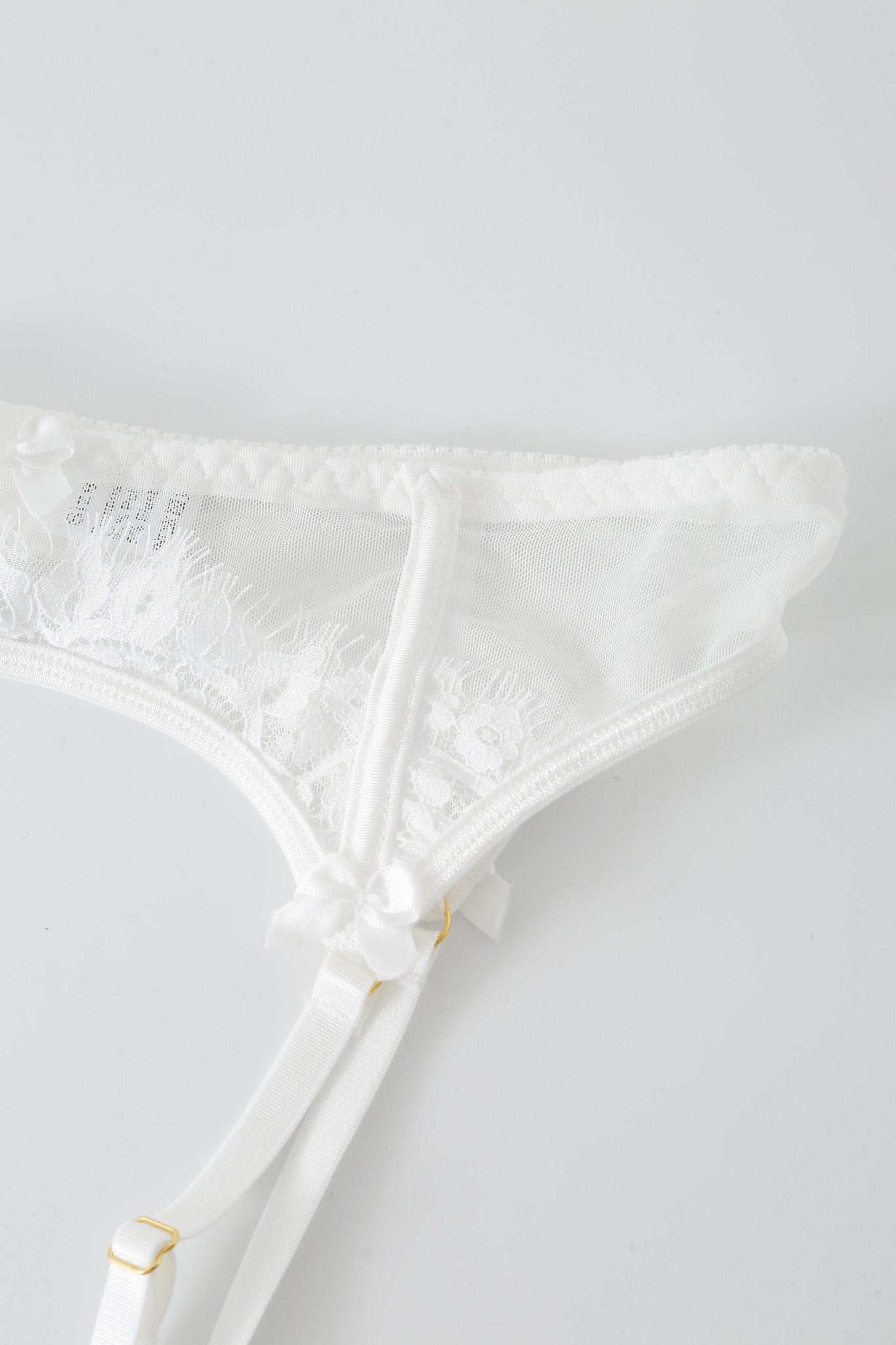 Close-up of the Eve w Mini Skirt- Full Set: a white lace garter belt adorned with floral patterns, dainty satin bows, and adjustable straps, showcased against a plain white background. This elegant lingerie set pairs beautifully with its included mesh mini skirt or other delicate pieces, featuring subtle rhinestone detailing for an extra touch of sparkle.