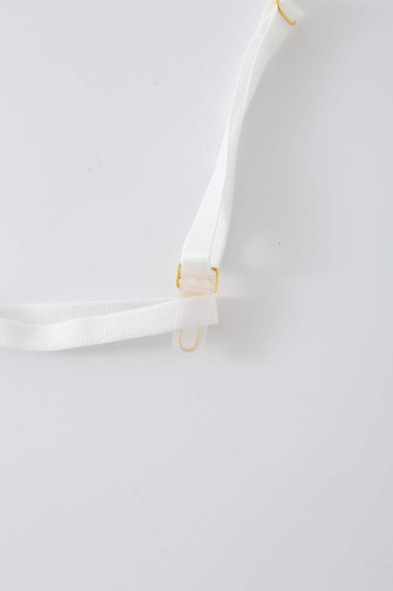 A detailed close-up of the Eve w Mini Skirt- Full Set’s white adjustable strap, showcasing its gold clip, clear plastic hook, and subtle rhinestone accents, all set against a plain white background.