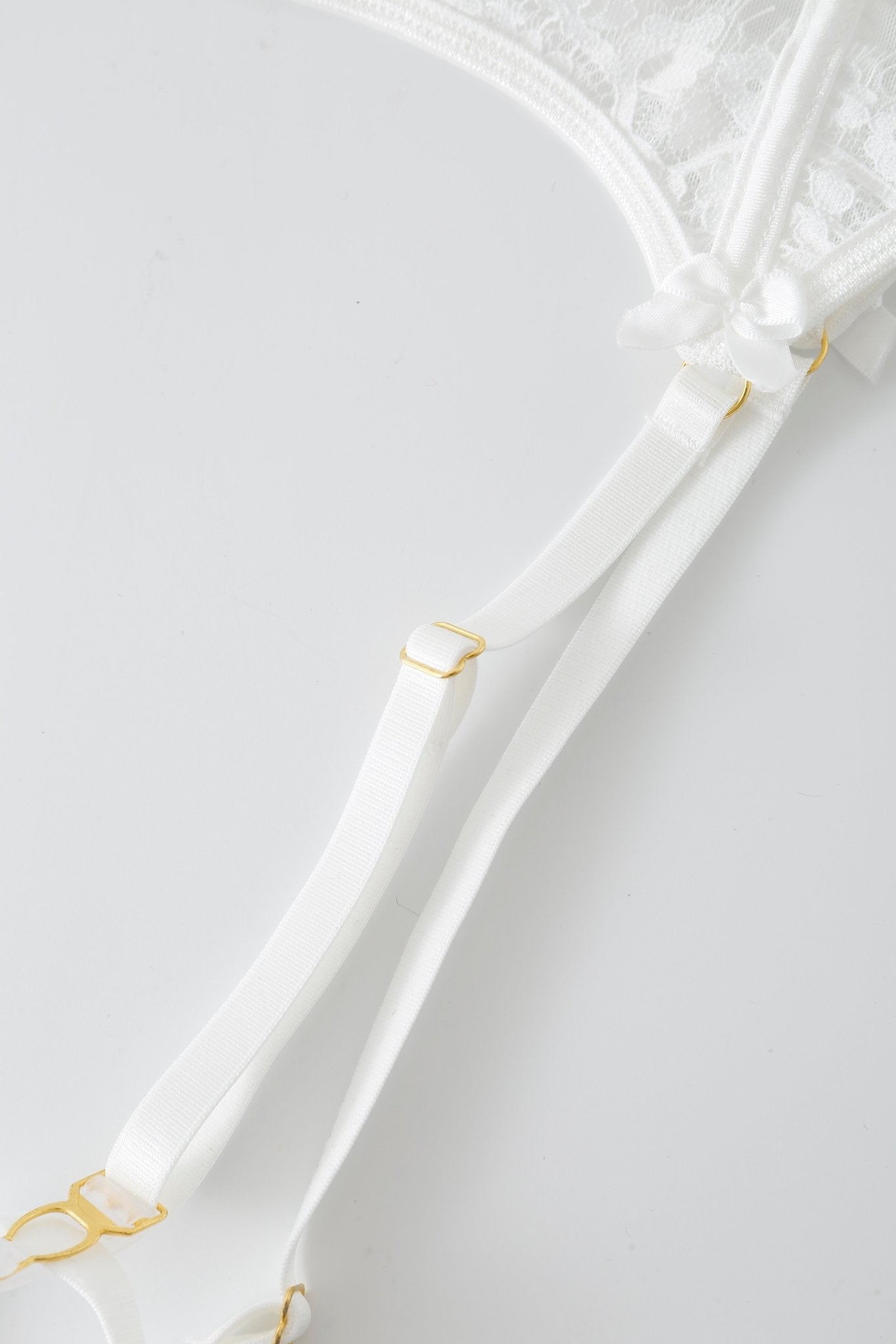 Close-up of the Eve w Pashmina- Full Set lingerie in white lace, featuring delicate straps and gold hardware, displayed on a plain light background.