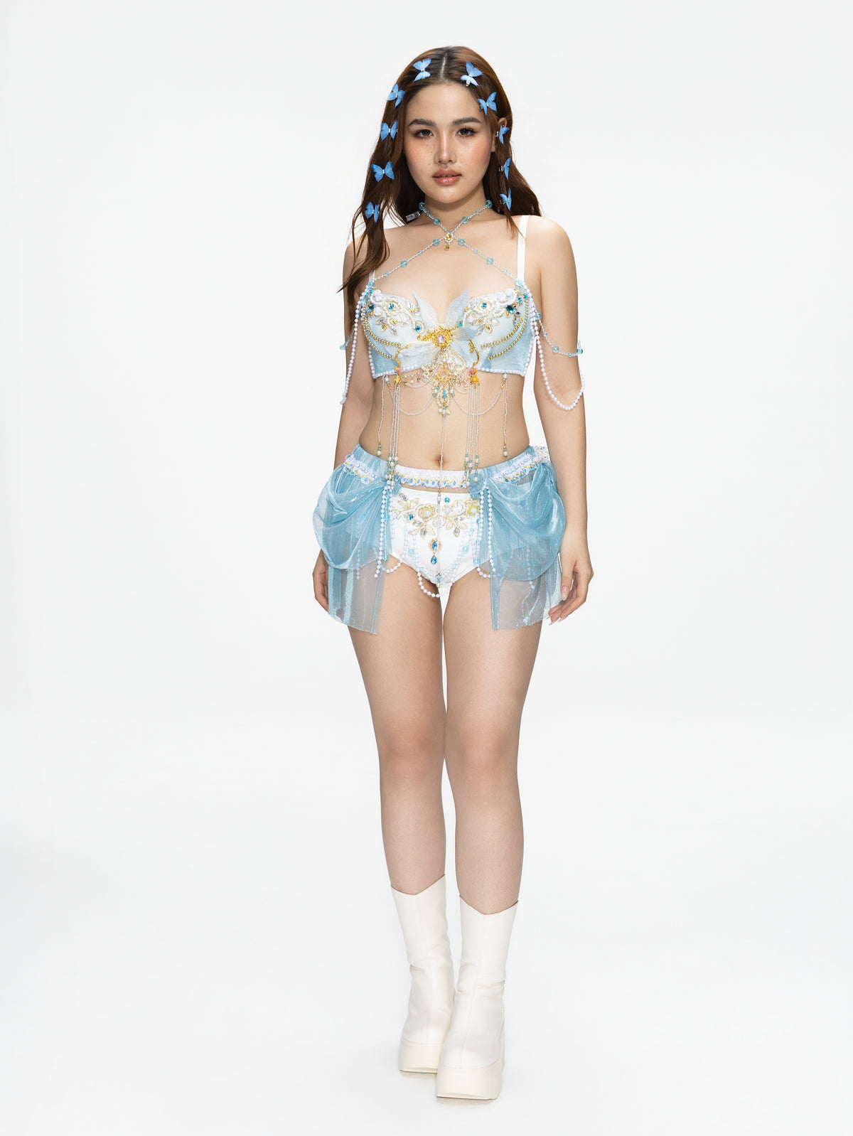 A woman stands facing forward, wearing the GOSSAMER - Top - Blue paired with coordinating accessories and white platform boots, against a plain white background.