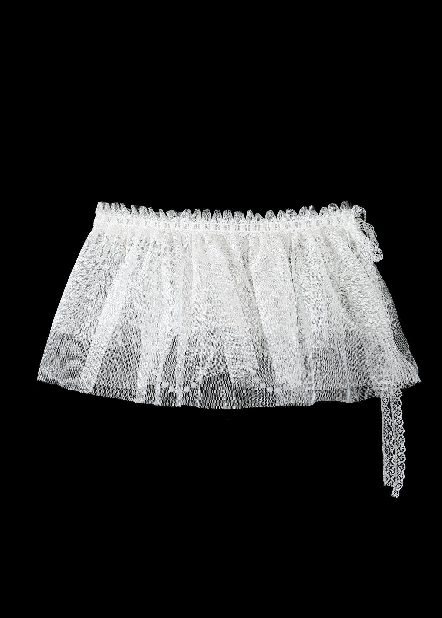 The Haló - White - Skirt features white lace and tulle with a polka dot pattern and ribbon detail, perfect for pairing with your favorite lace bodysuit or as a chic addition to any festival look. Shown against a black background.