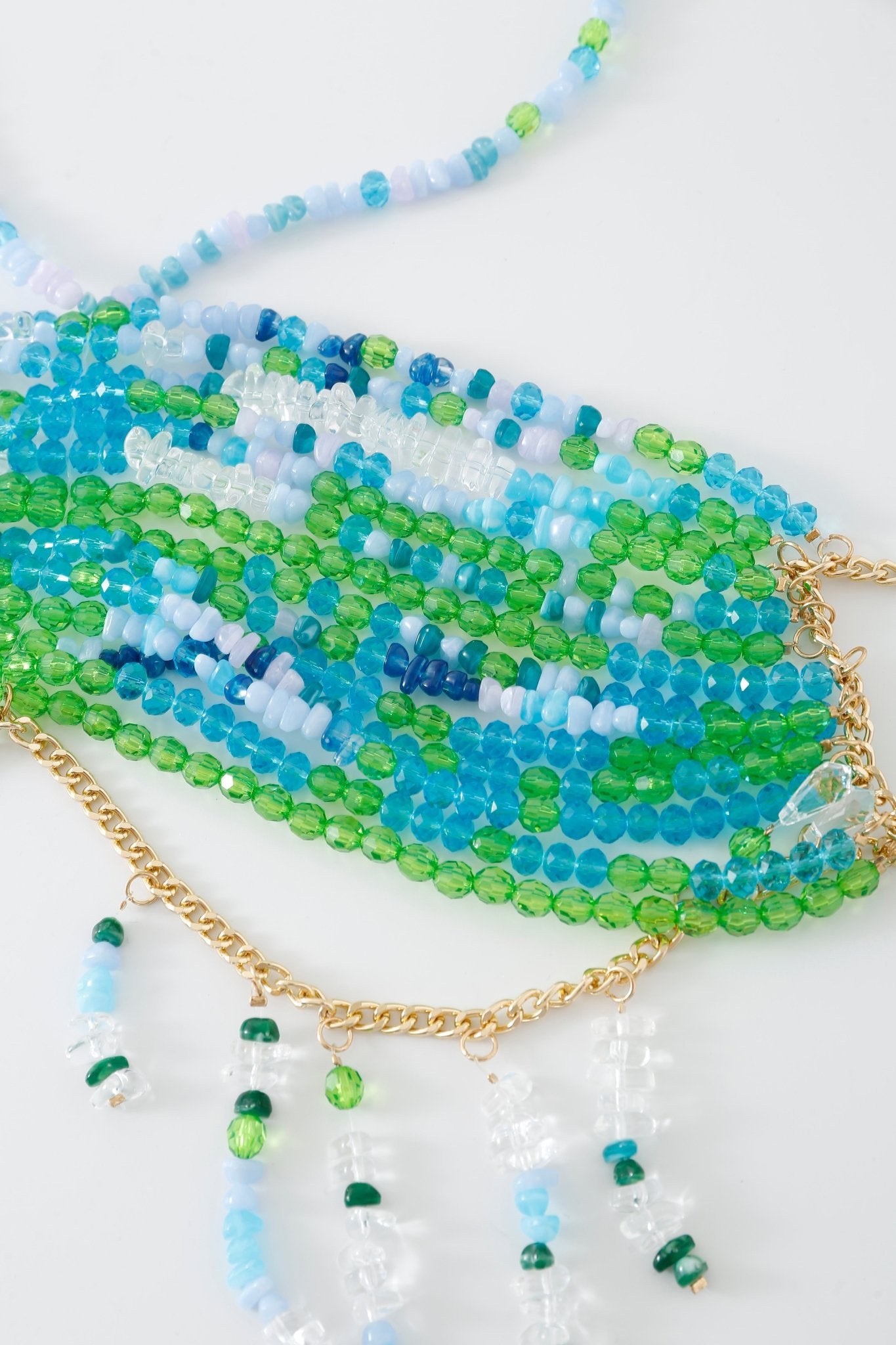 The Lagoon w Pashmina- Full Set features multiple beaded necklaces in shades of blue, green, and clear, accented with gold chain details reminiscent of a fringe pashmina wrap, arranged on a white background.