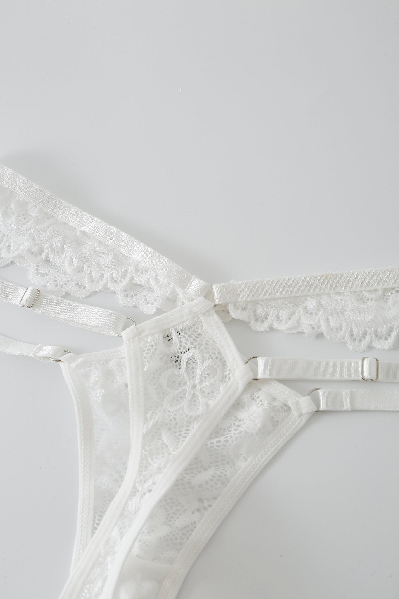 The Mariposa w Mini Skirt- Full Set, a white lace lingerie ensemble with adjustable straps and delicate rhinestone detailing, is laid flat on a white surface.