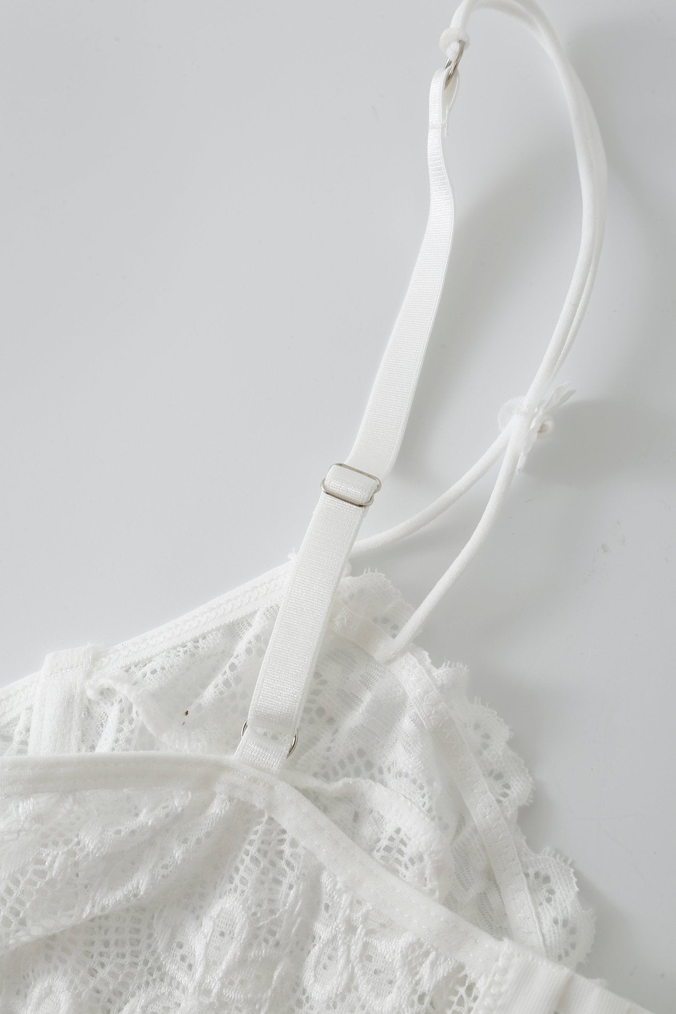 Close-up of the Mariposa w Pashmina- Full Set, a white lace garment featuring adjustable shoulder straps, laid on a white surface.
