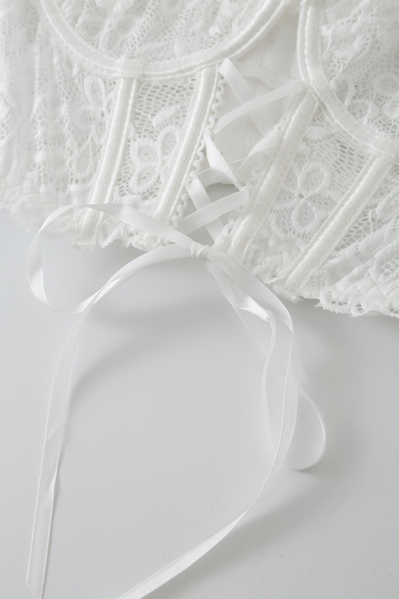 Close-up of a white lace garment with ribbon details and a tied bow, displayed on a white surface—perfectly complementing your Mariposa w Mini Skirt- Full Set.