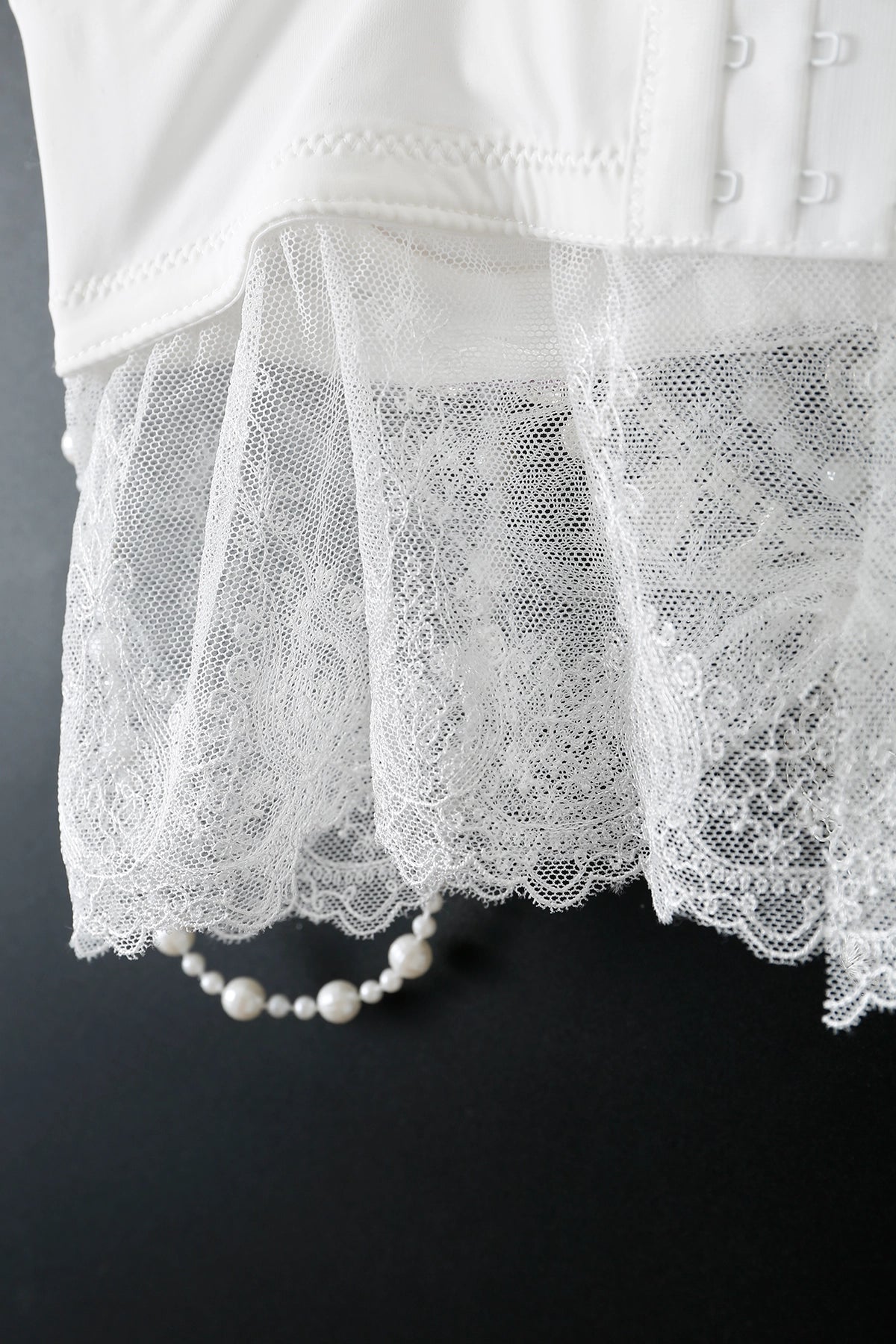 A close-up of the Ondine - Full Set - Purple, featuring intricate lace and hook-and-eye closures beside a pearl bracelet—an elegant choice to elevate your handmade rave outfit.