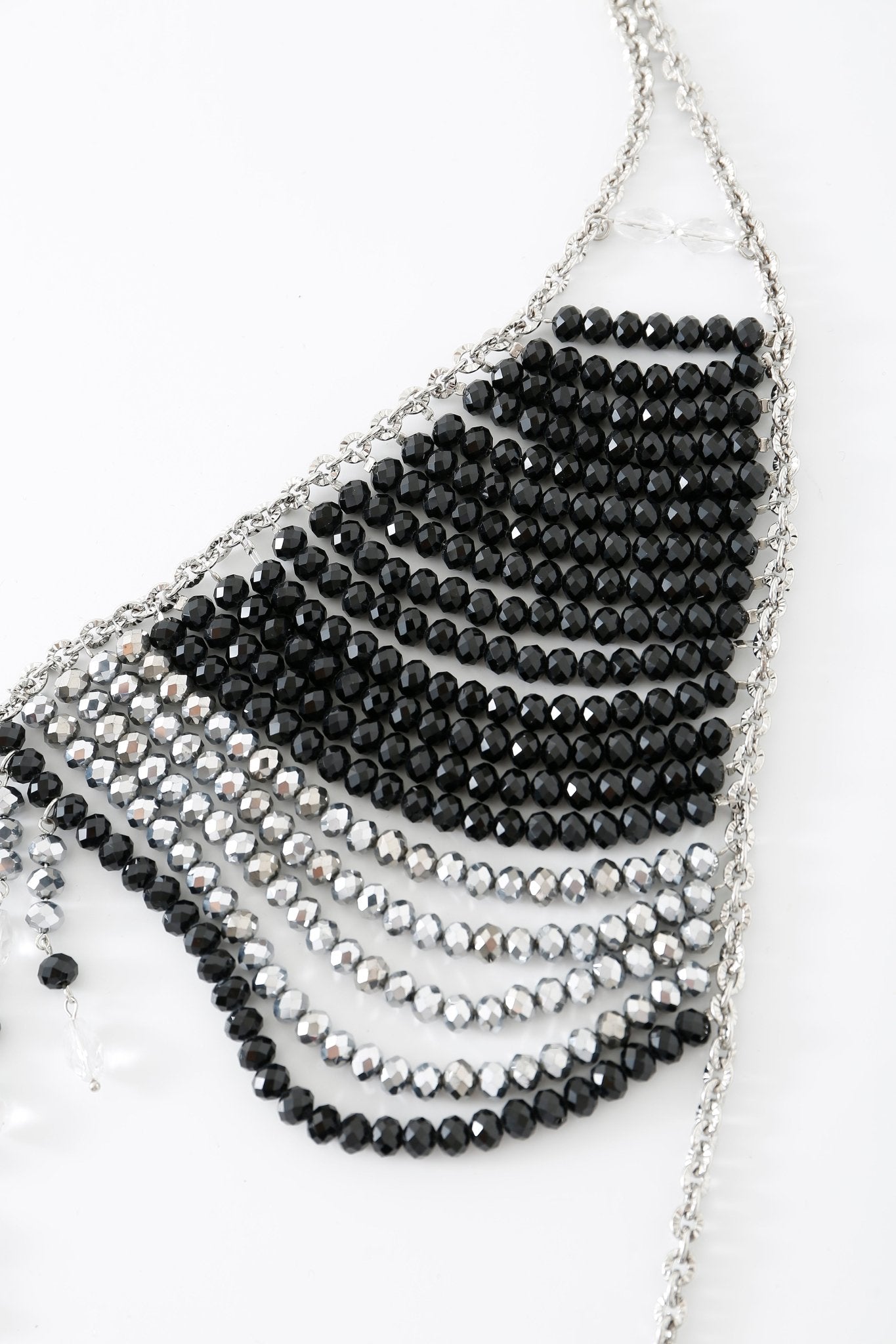 The Onyx w Pashmina- Full Set features an accessory with alternating rows of black and silver beads, arranged in a triangular pattern reminiscent of the intricate detailing found on a beaded top, beautifully displayed on a white surface.