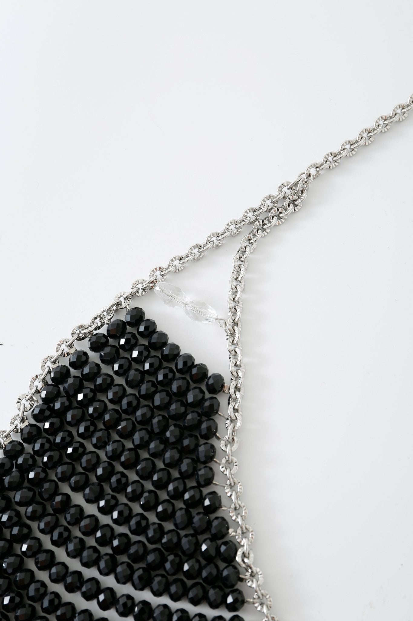 A close-up of the Onyx w Pashmina- Full Set showcases a silver chain necklace featuring faceted black beads arranged in a striking triangular pattern on a white background, echoing the elegant detailing seen in beaded tops and Onyx lingerie.