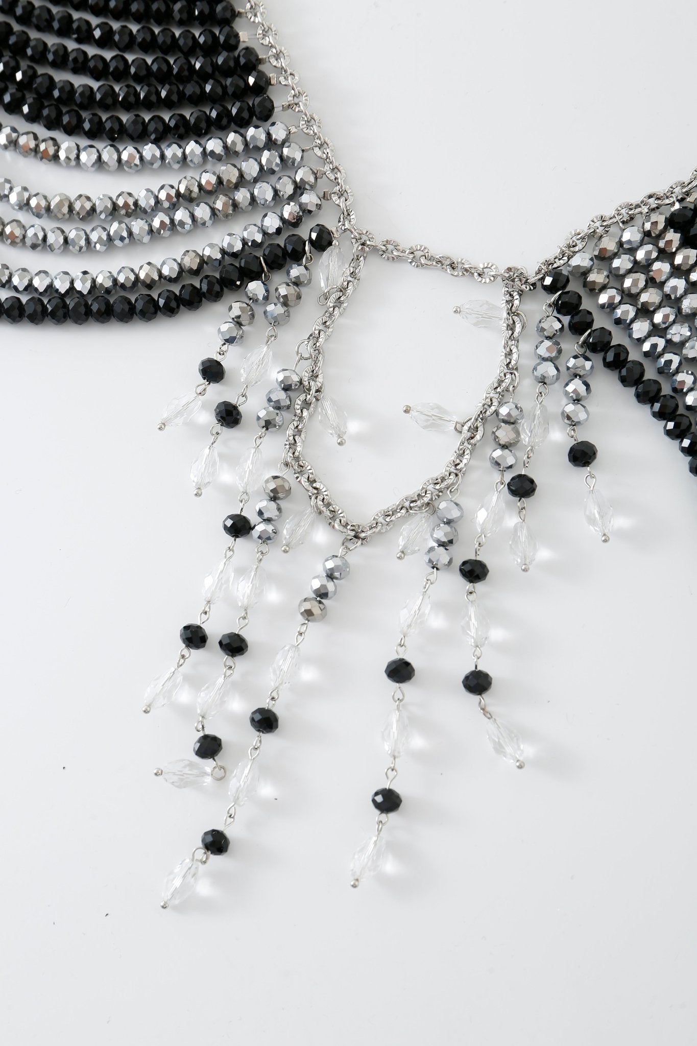 A close-up of the Onyx w Pashmina- Full Set showcases black, silver, and clear beads arranged in cascading strands on a white background, echoing the intricate detailing found on a beaded top.
