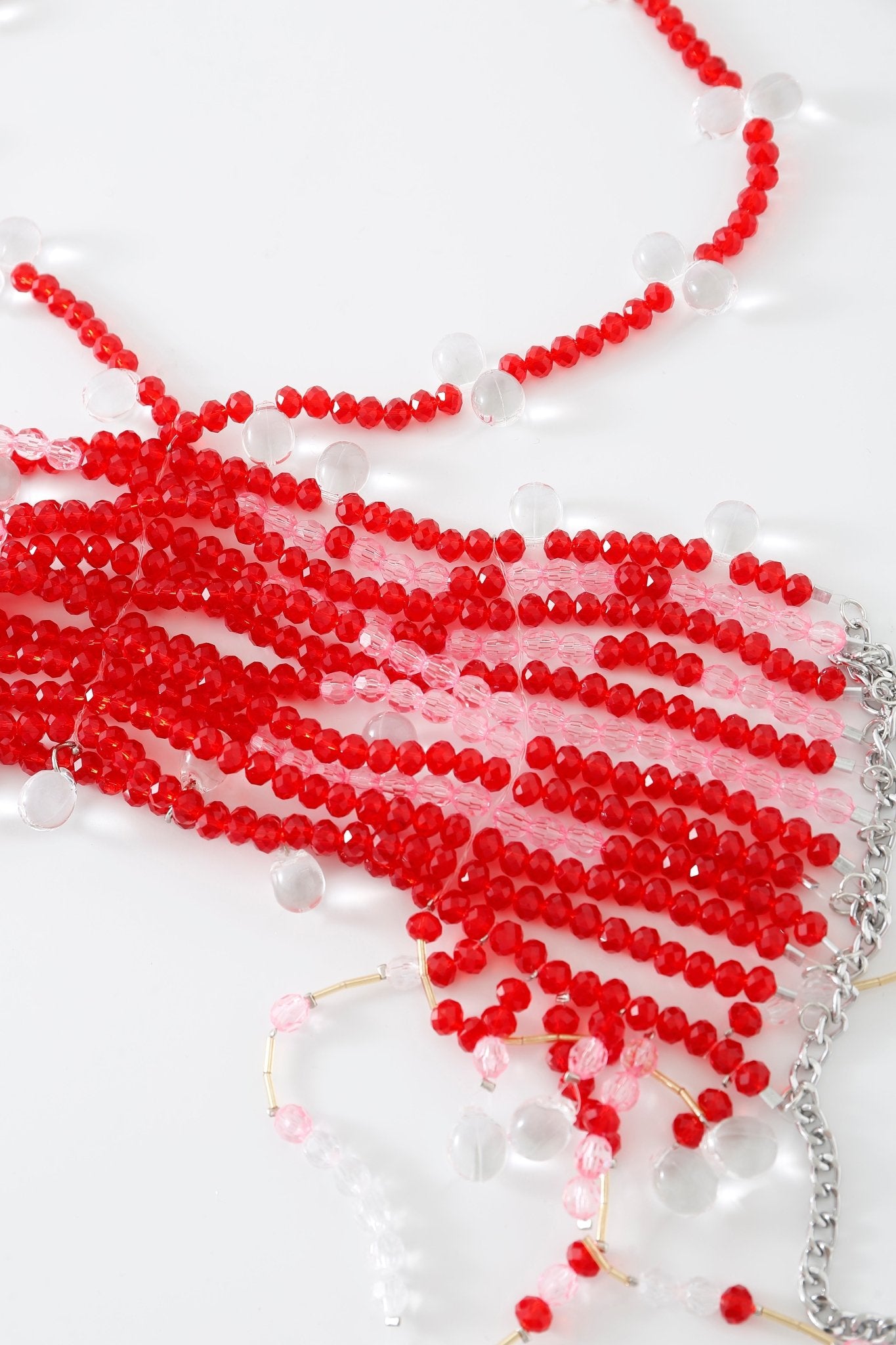 The Poppy w Pashmina- Full Set, featuring multiple red and clear beaded necklaces—some adorned with chain links reminiscent of a beaded top—is arranged on a white surface in a slightly tangled display.