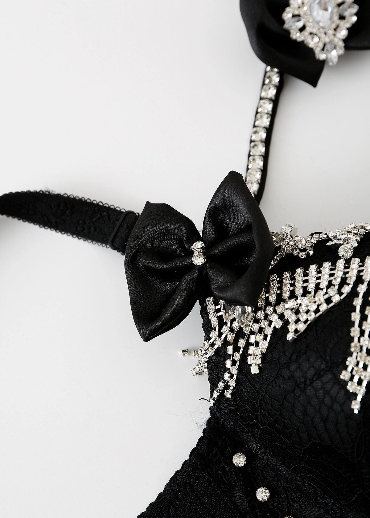 Close-up of the Swan-Black-Top, a handmade lace bra with rhinestone embellishments, sparkling fringe, and a black satin bow in the center—a perfect festival bra top.