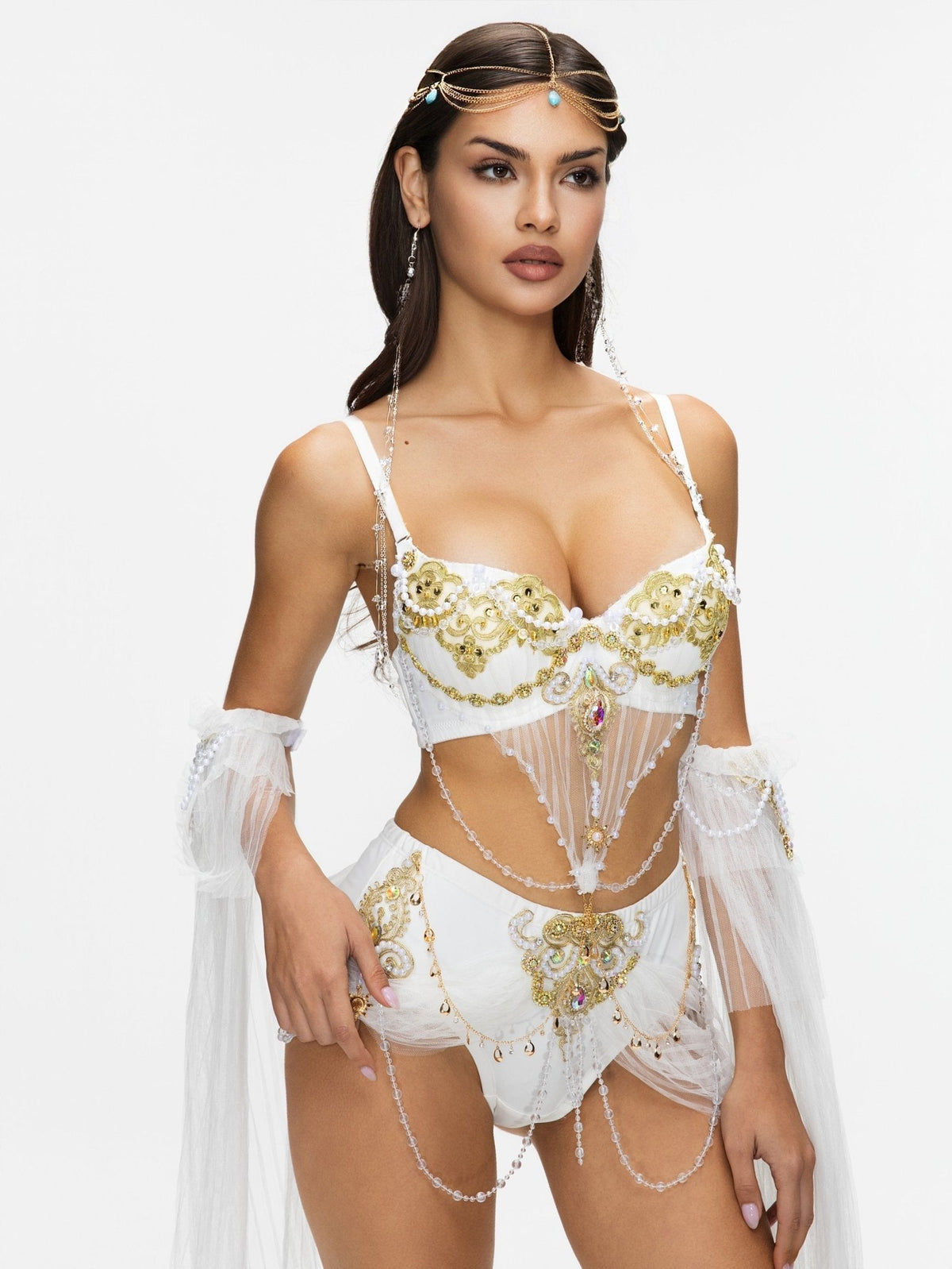 A woman stands against a plain white background wearing the REVERIE - White - Bottom, styled with sheer drapes, ornate gold embellishments, jewelry, and a headpiece.