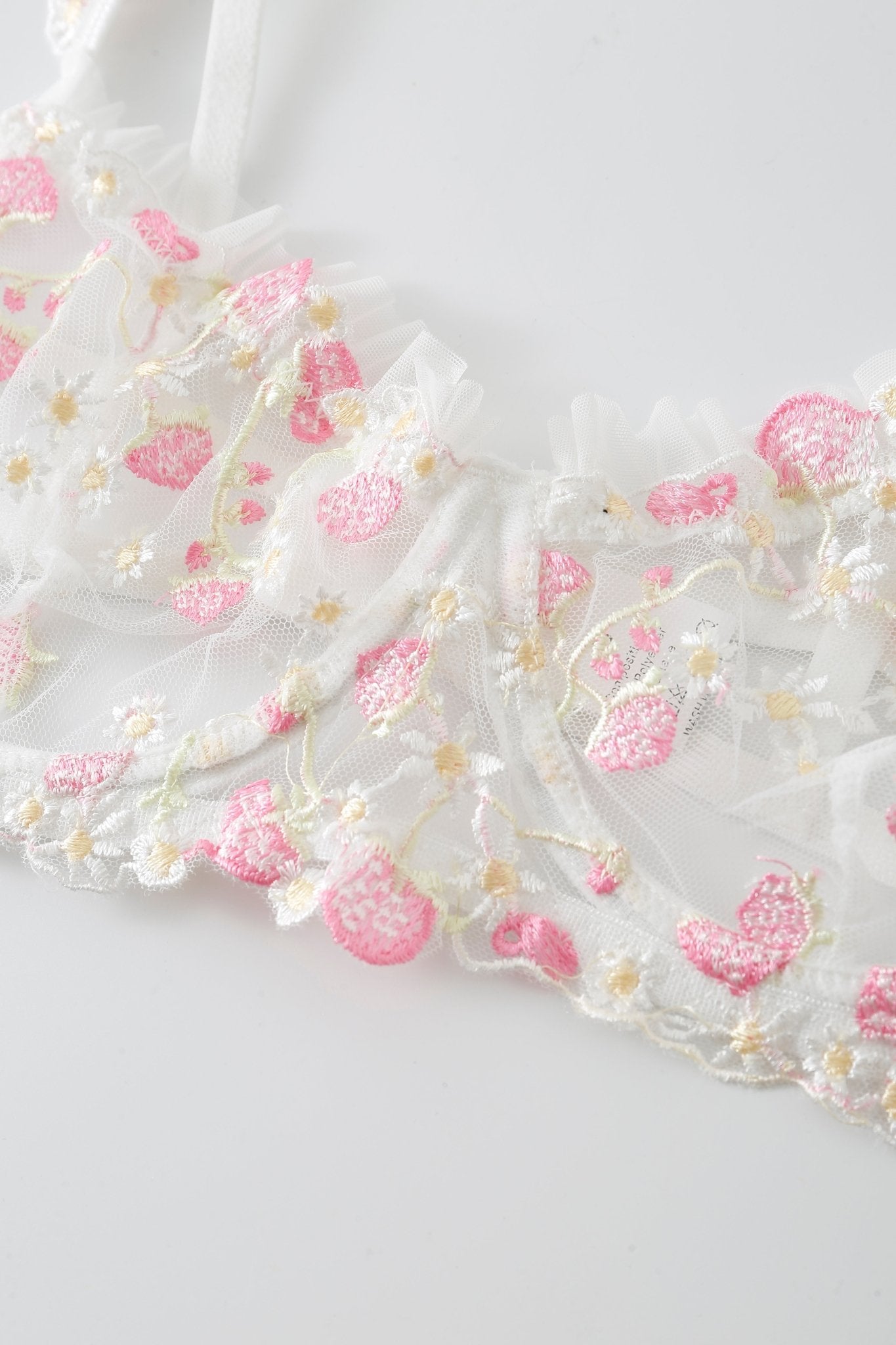 Close-up of the Rosette w Pashmina- Full Set, featuring white lace fabric adorned with pink and yellow embroidered flowers and hearts, a sheer ruffled edge, and photographed on a white background.